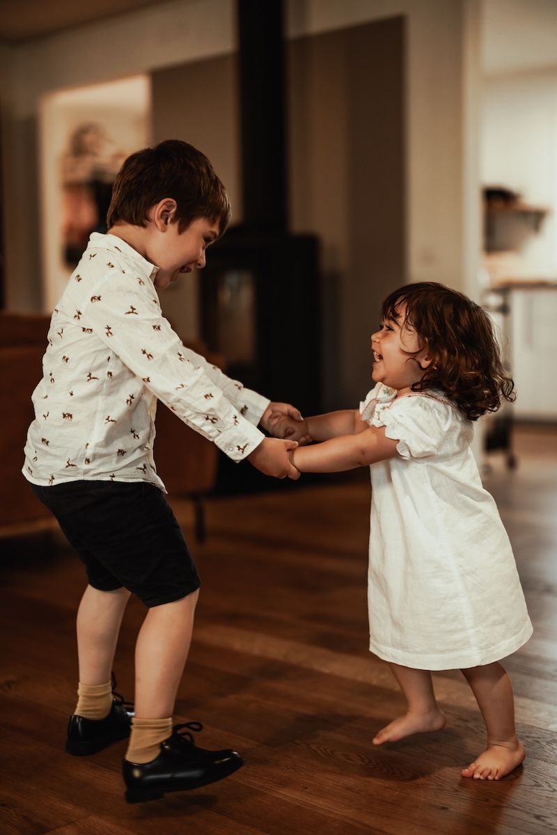 Två små syskon håller händer och dansar under en familjefotografering i hemmet. Foto: Grevholm Photography.