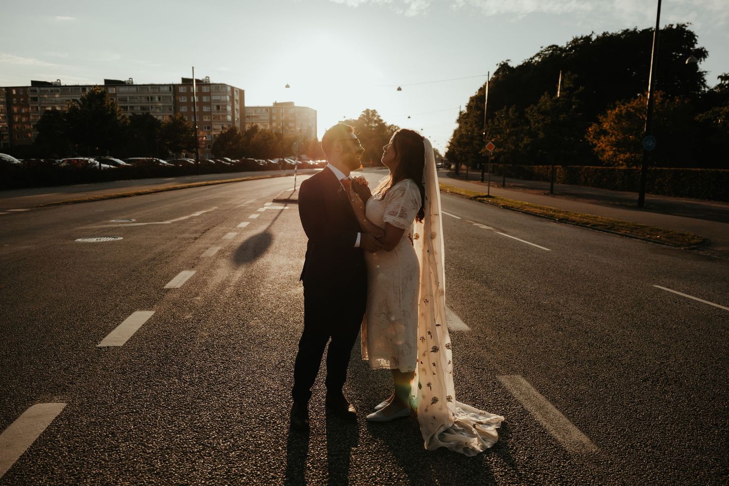 Brudpar omfamnar varandra och pussas mitt på gatan i Malmö under solnedgång. Foto av Grevholm Photography.