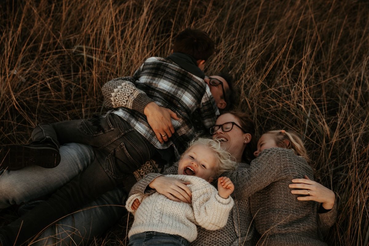 En familj busar i det höga gräset på sanddynorna under en familjefotografering i Laholm. Foto: Grevholm Photography.