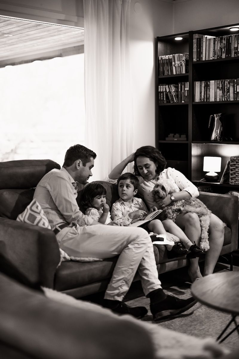En familj sitter i soffan och läser under en familjefotografering i hemmet. Foto: Grevholm Photography.