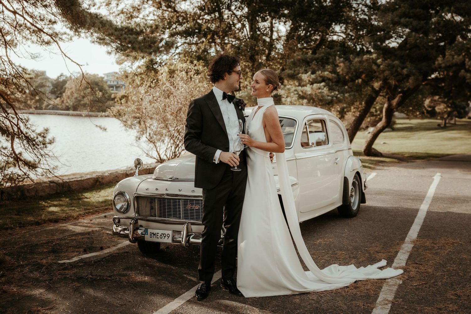 Brudpar står framför en gammal bil och skålar i champagne under deras höstbröllop på Särö. Fotograf Grevholm Photography.
