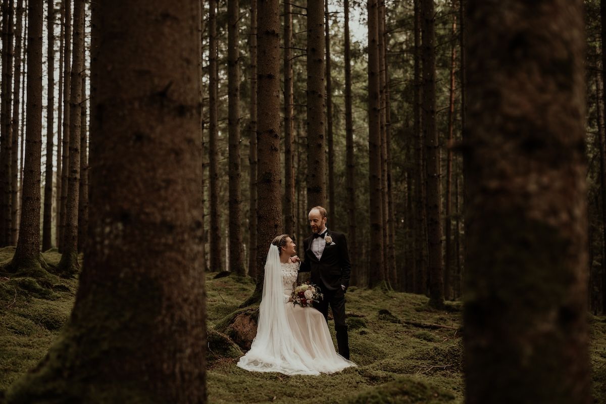 En kvinna iklädd brudklänning sitter på en sten i en skog. Hennes nyblivna make står bredvid henne.
