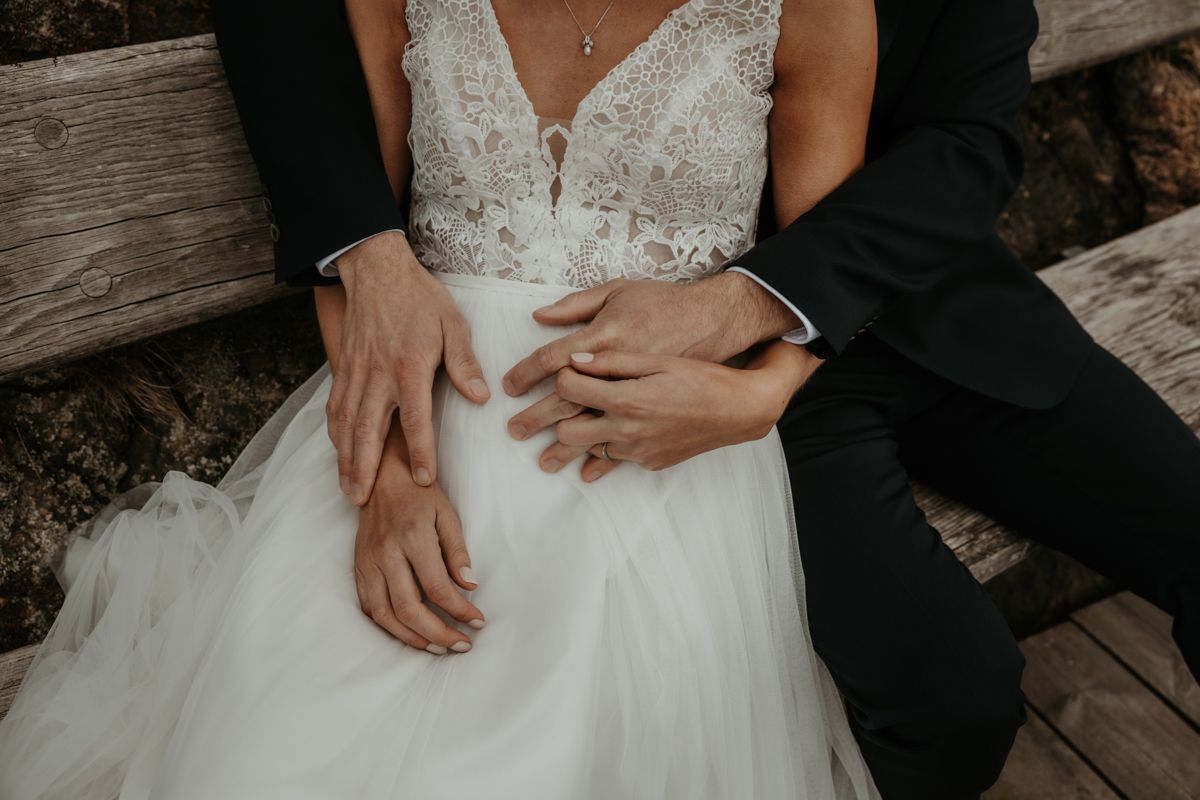 Närbild på brudpars händer som sitter på en bänk i Nösund under deras västkustbröllop. Fotograf Grevholm Photography.