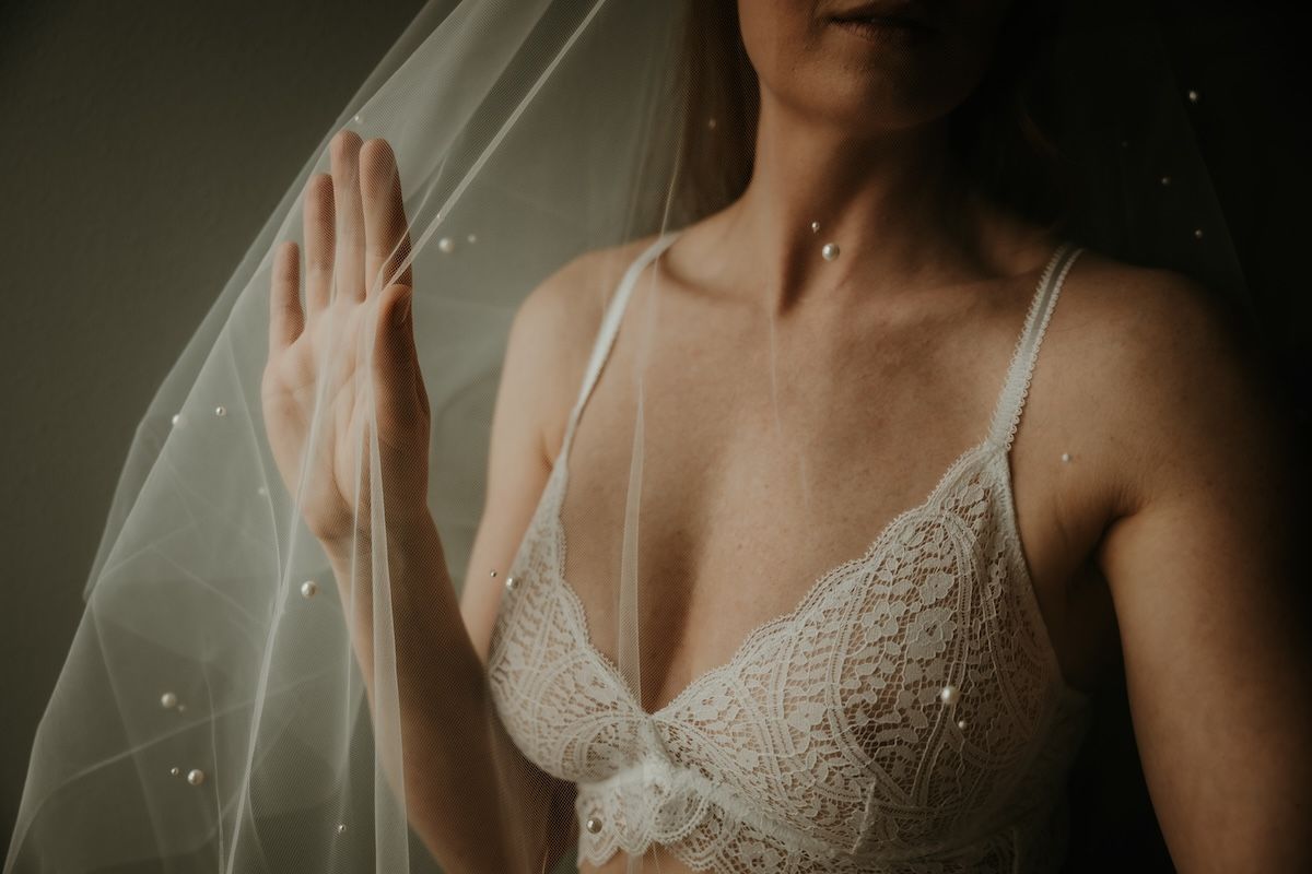 Boudoirfotografering med blivande brud som står under sin slöja. Foto Grevholm Photography.