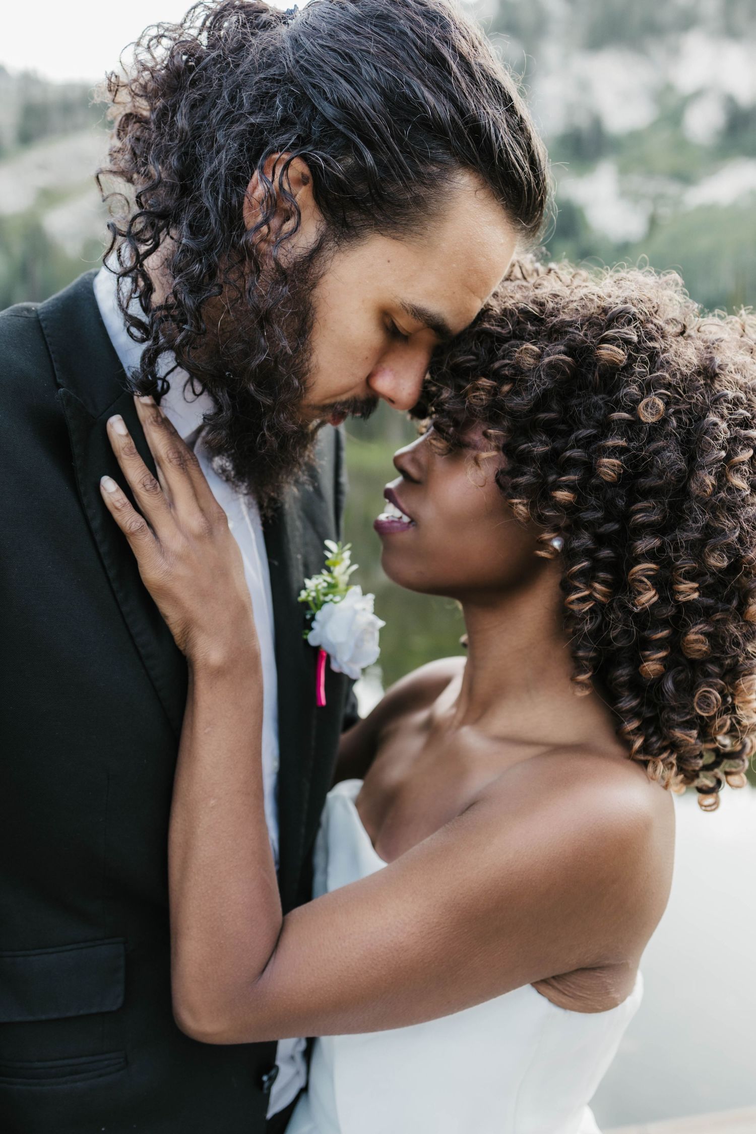 A romantic wedding couple embraces tenderly outdoors, with the groom wearing black and bride in white.