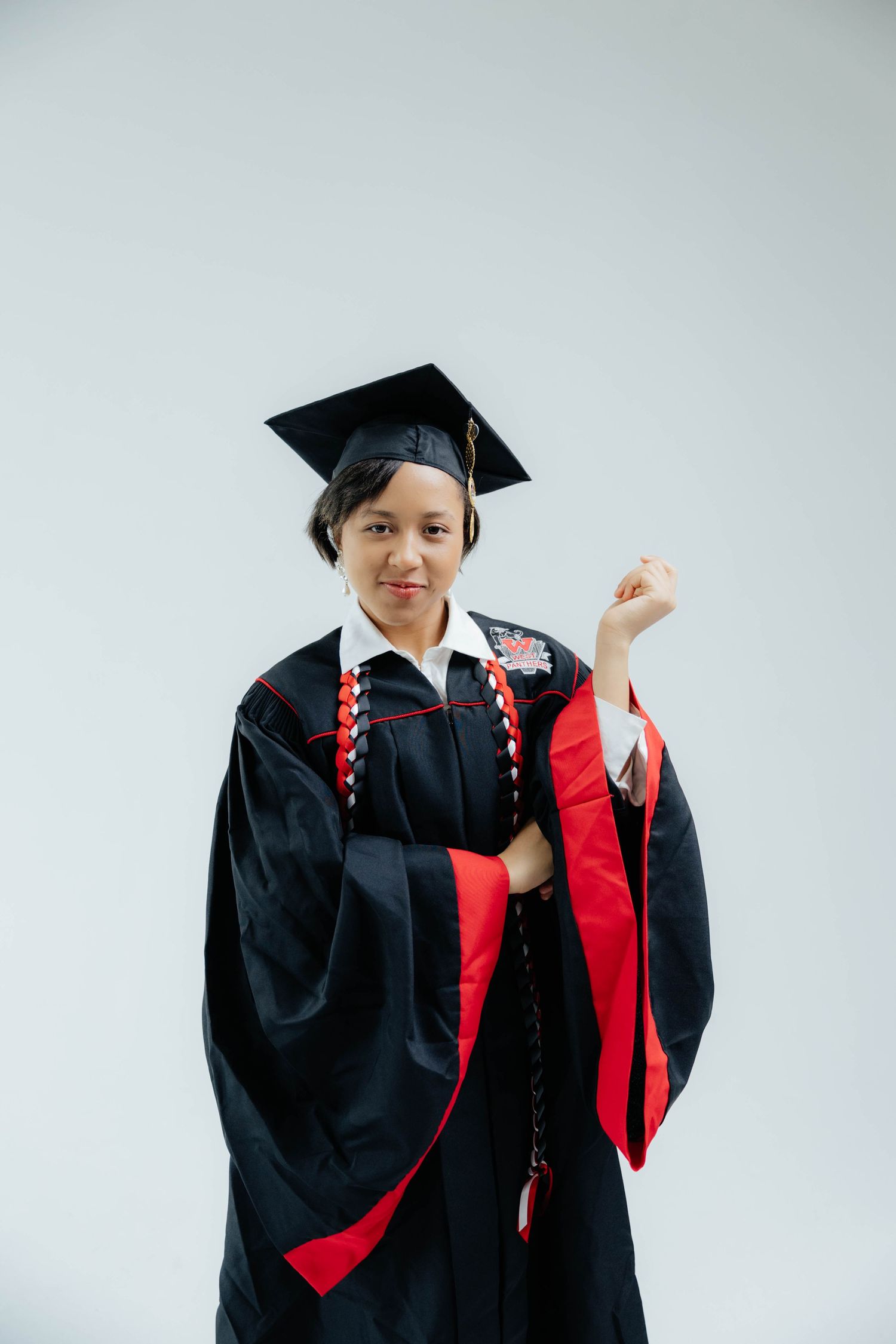 Graduate in black and red academic regalia poses against white background during commencement ceremony.