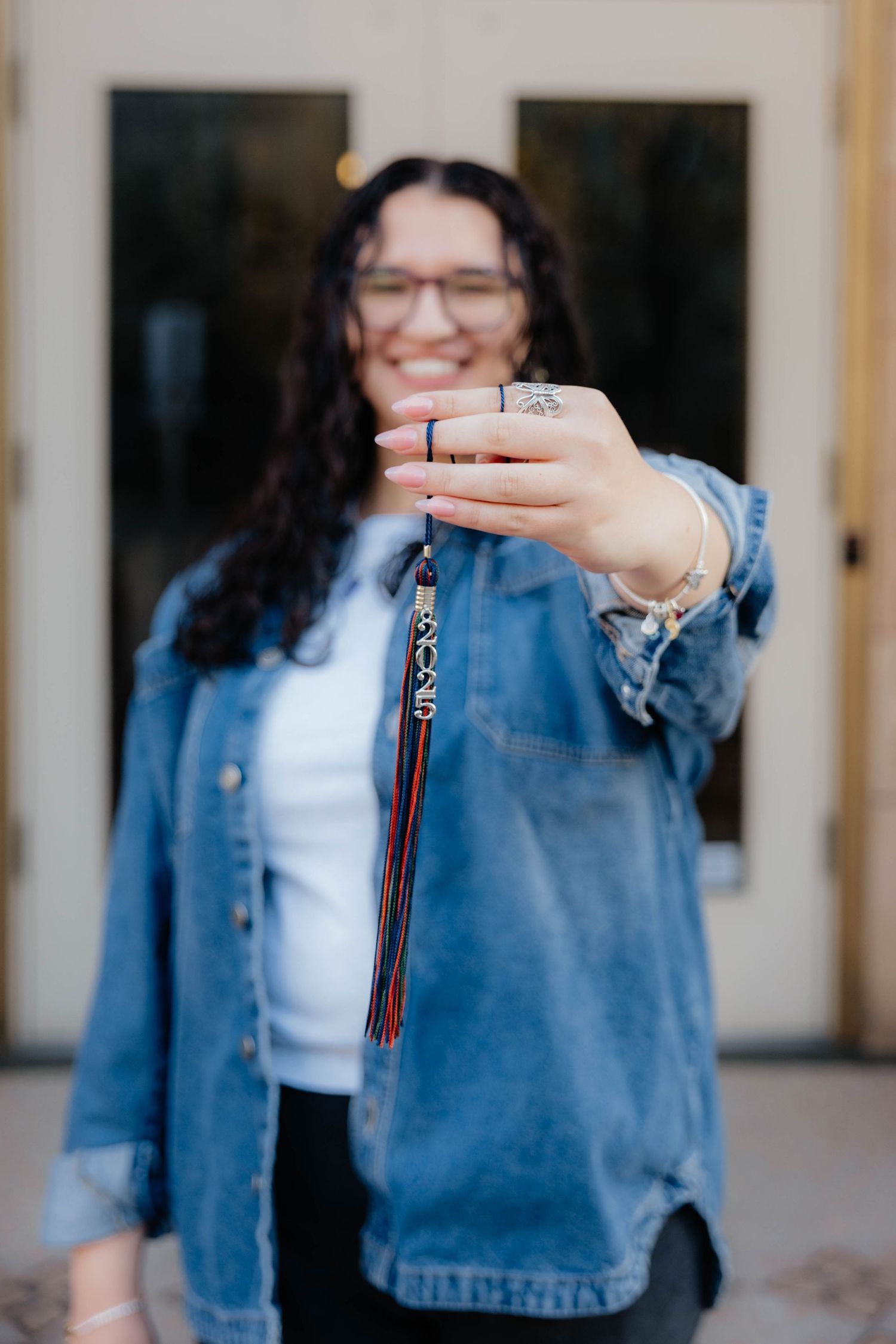 Graduate holds up tassel while wearing denim jacket and white shirt.