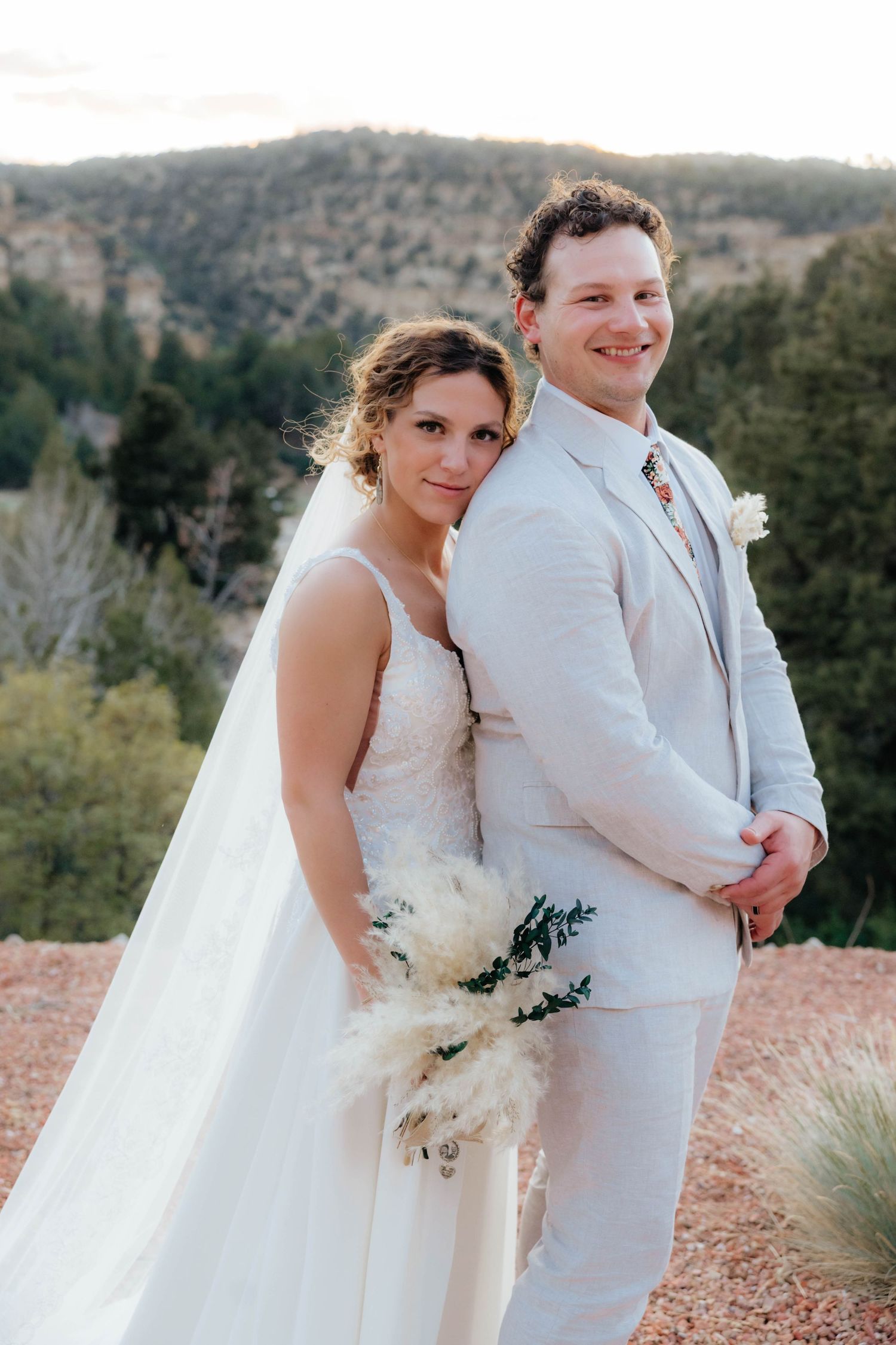 Wedding couple poses together in white attire against a desert landscape backdrop.