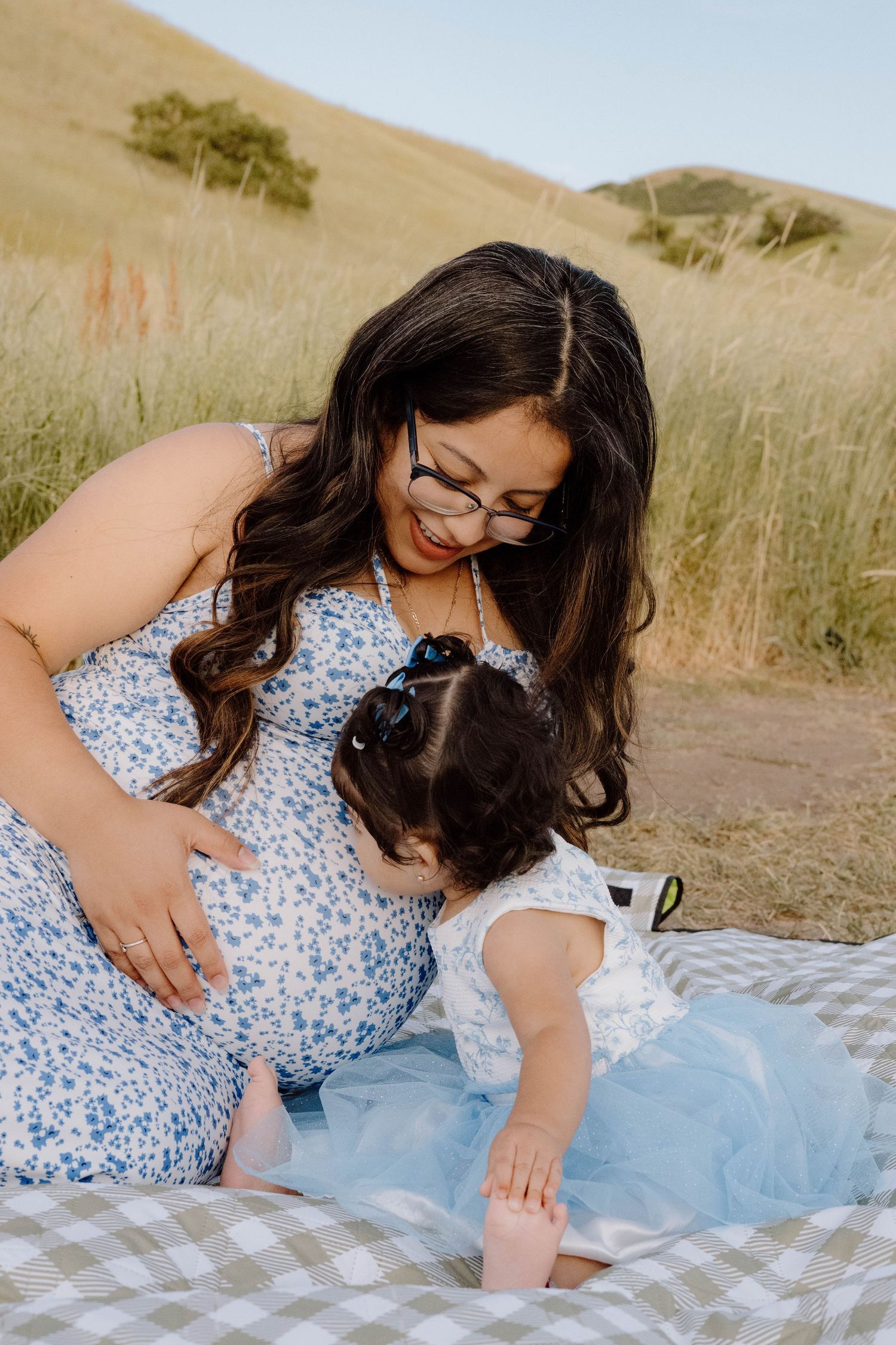 A maternity photo session on a picnic blanket in a sunny meadow.