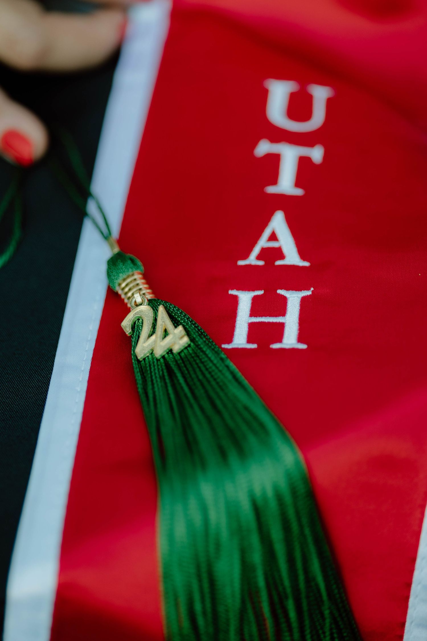 Close-up of green graduation tassel against red UTAH sash.