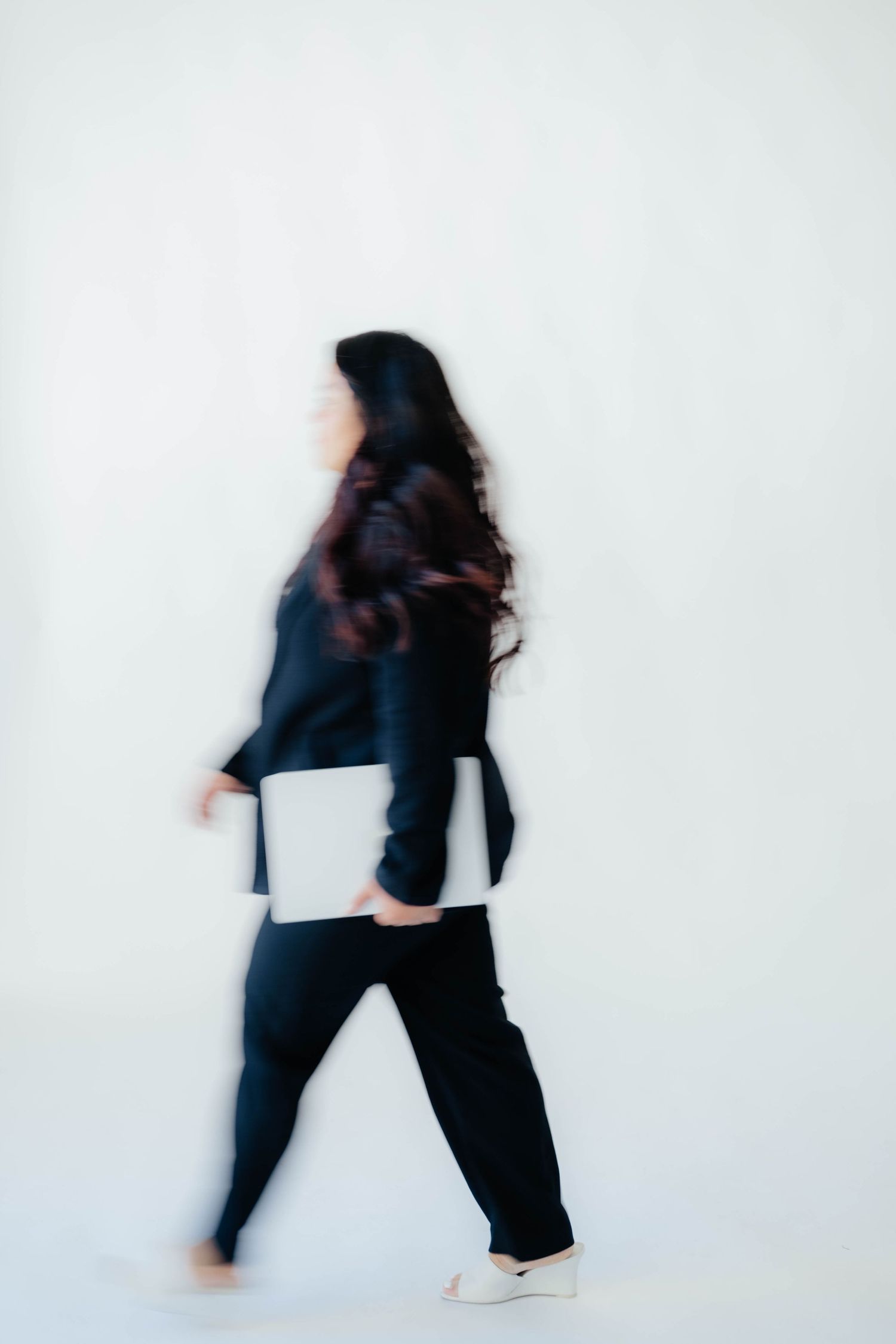 Motion blur photograph of person walking in black outfit against white background.