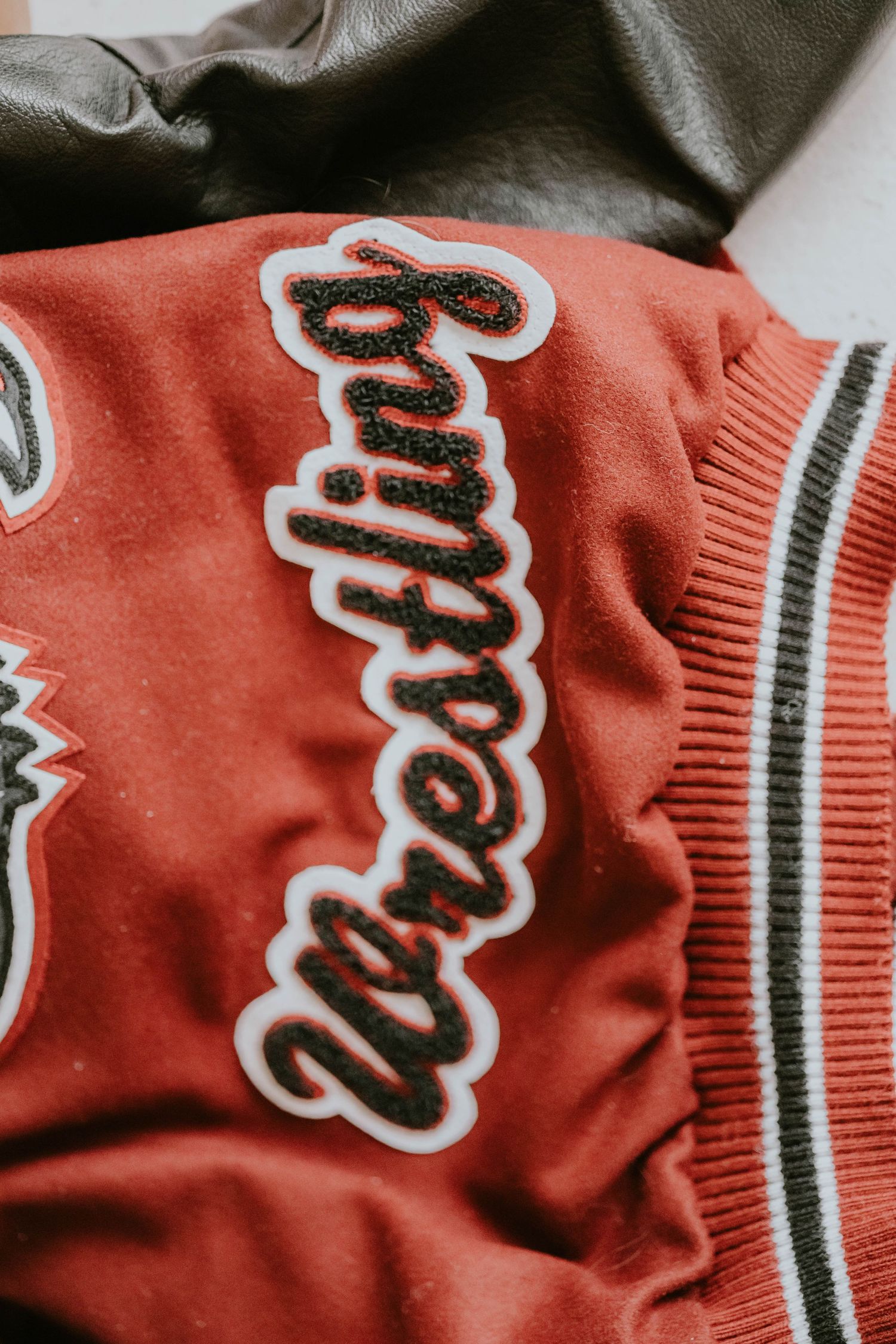 Detail shot of red varsity jacket showing embroidered lettering and striped trim.