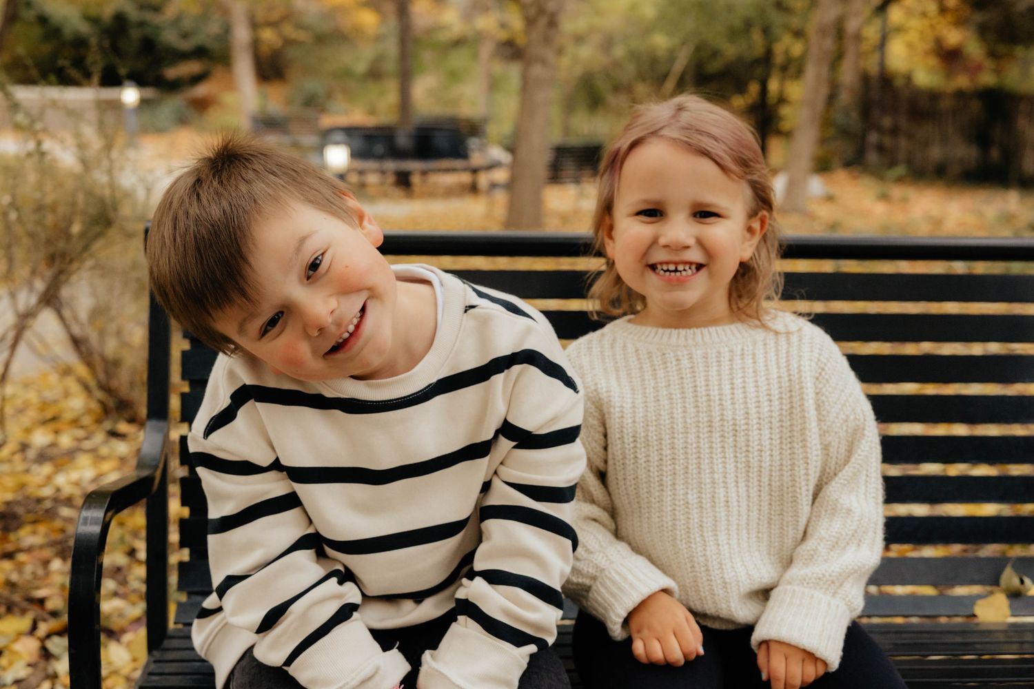 Family sitting together on wooden bench during autumn photo session.