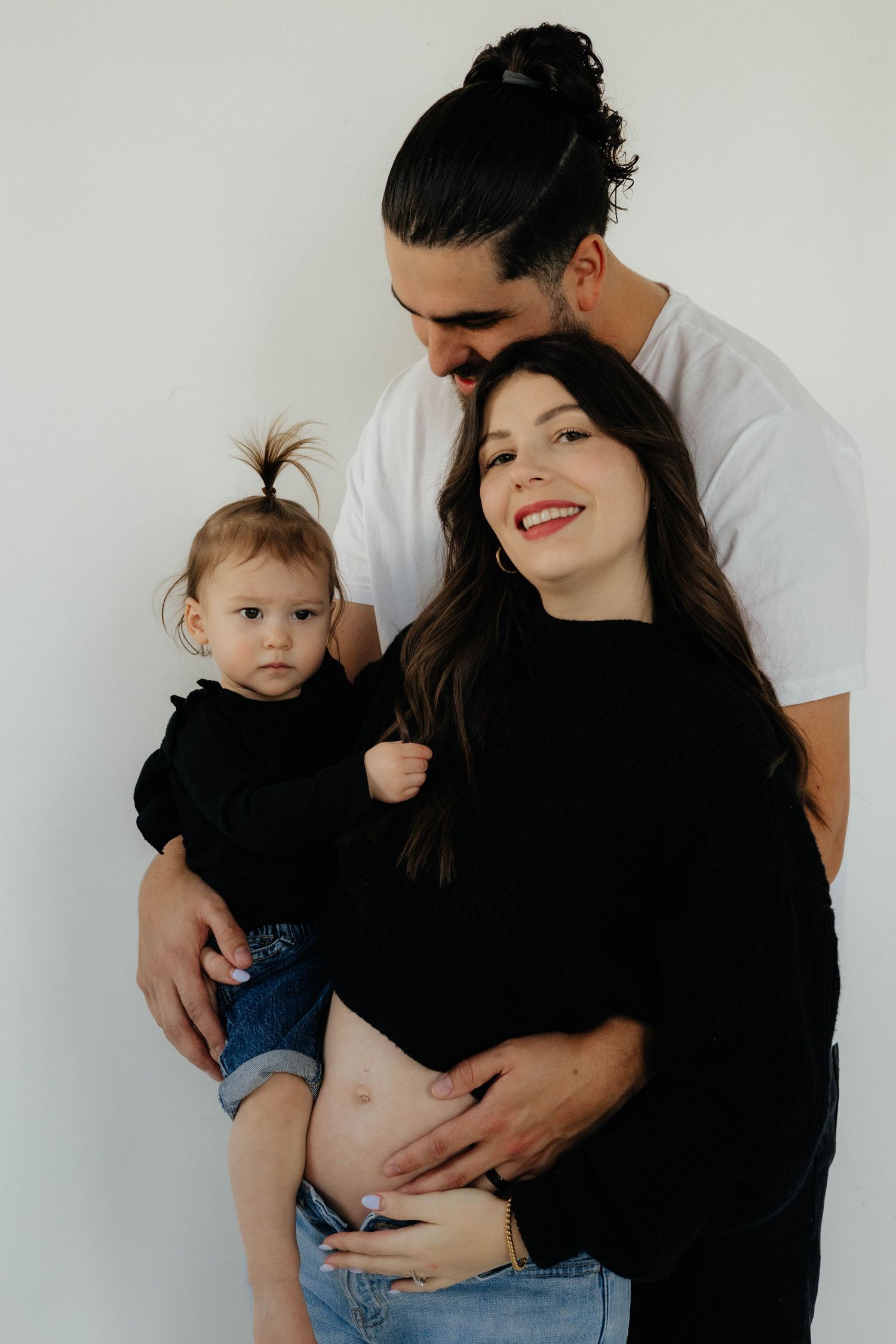 An intimate family portrait session with parents and baby in casual attire against white background.