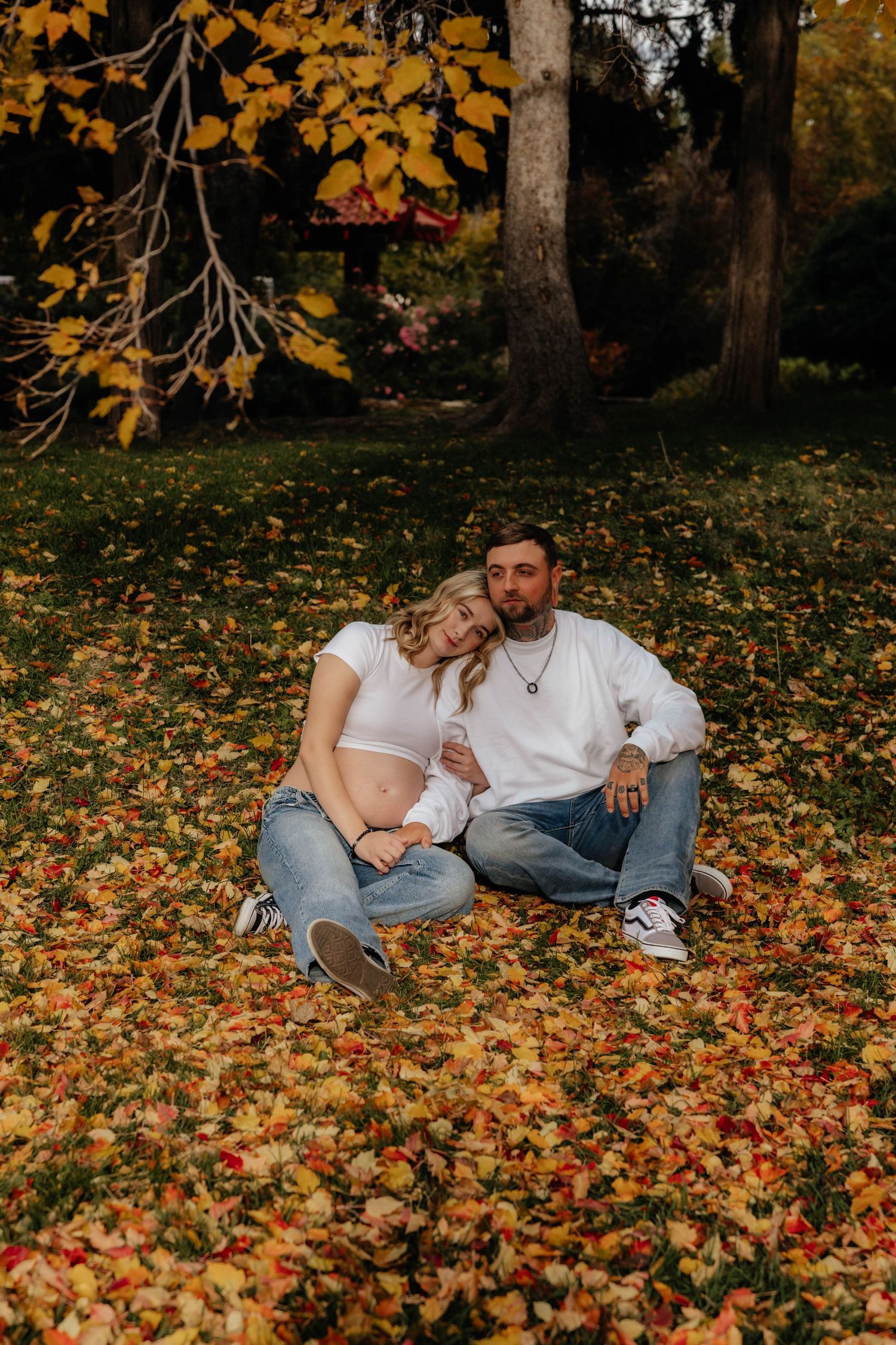 Couple lying on autumn leaves during outdoor maternity photoshoot with golden foliage.