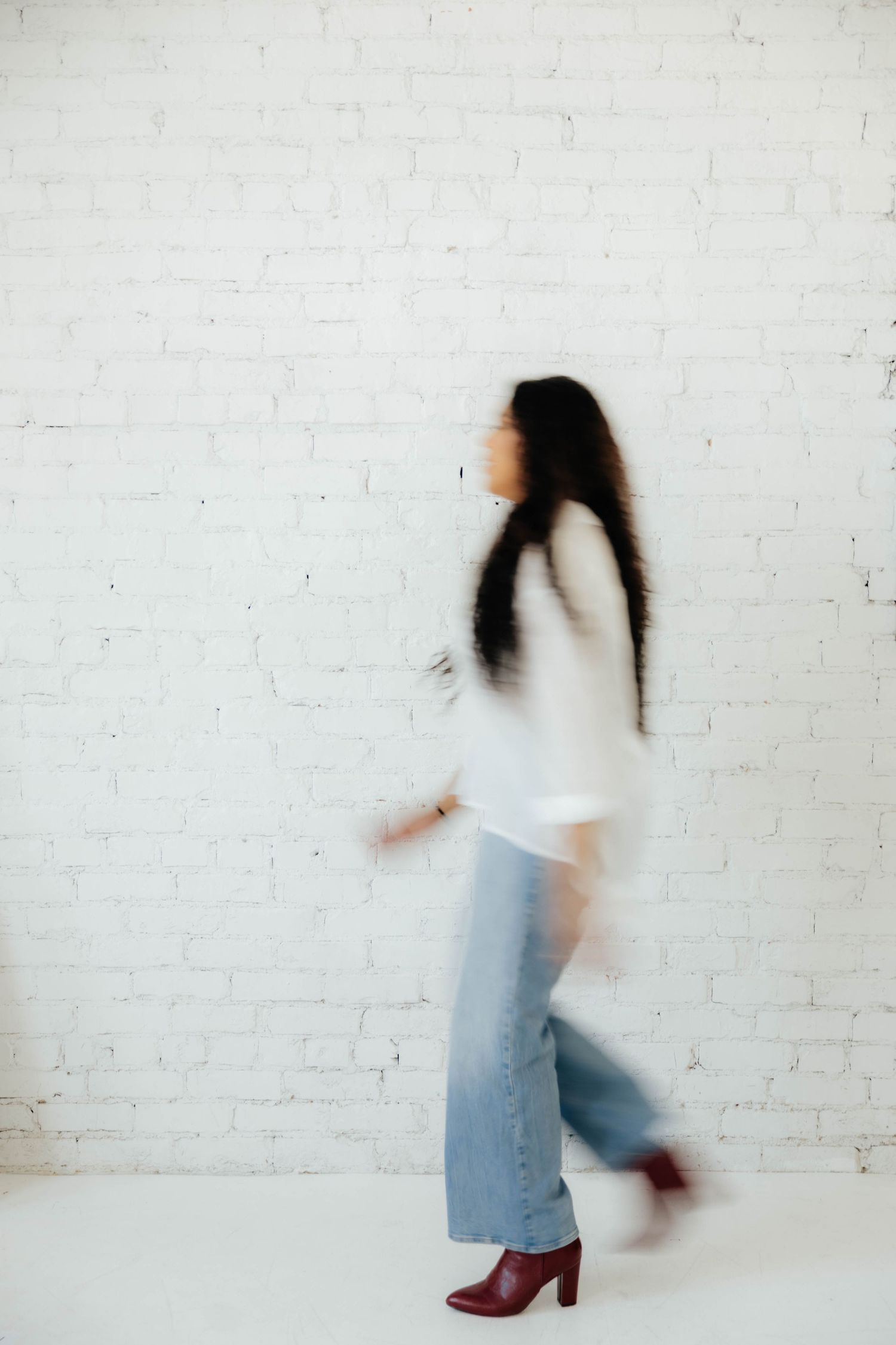 Motion blur photos showing someone in white top and jeans walking against a white brick wall.
