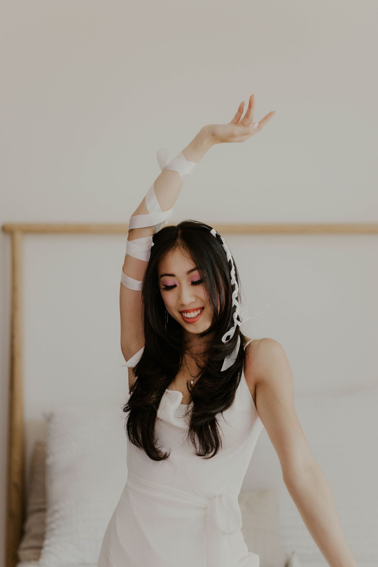 Joyful dance poses in white dress against minimalist studio backdrop.