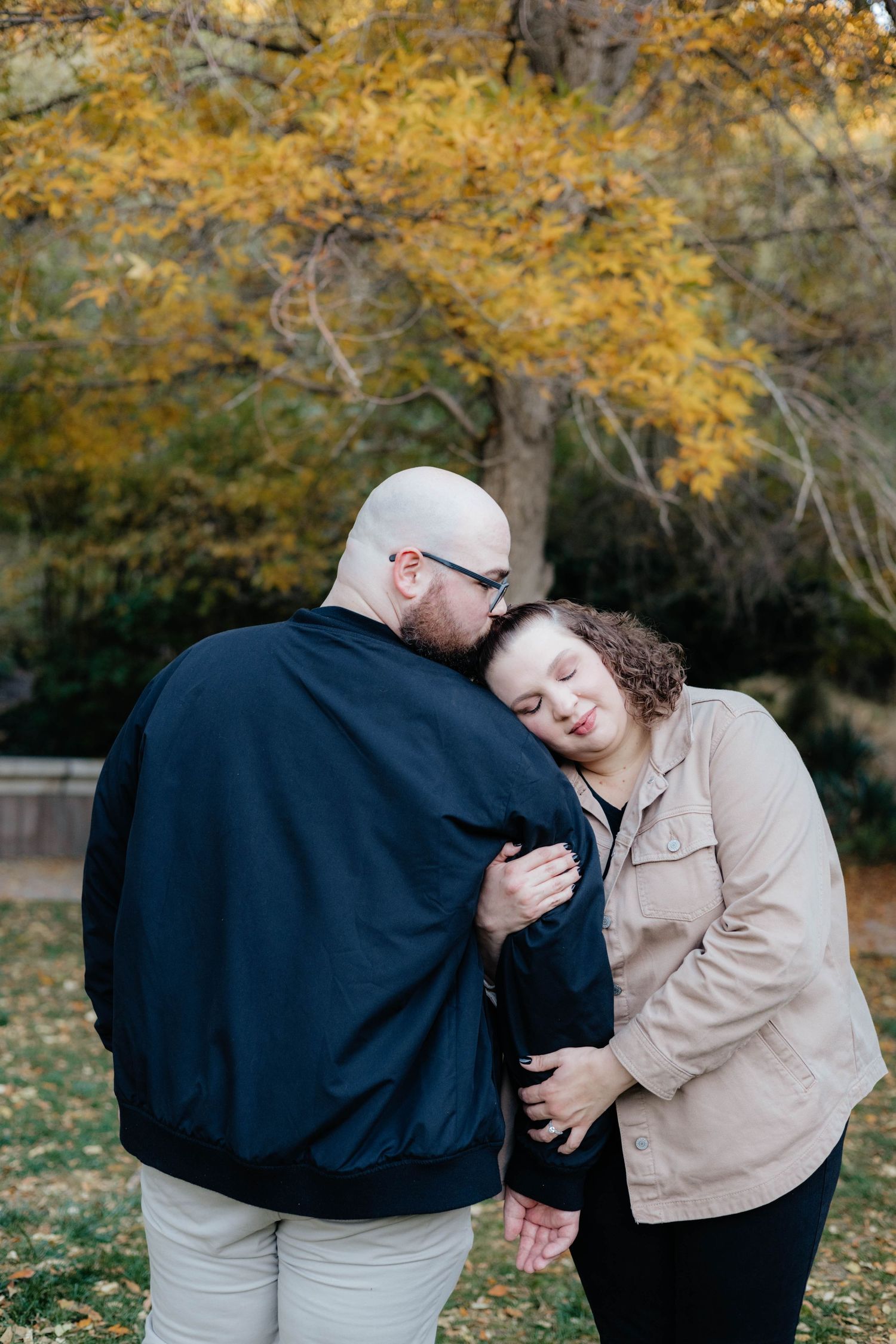 Couple sharing tender moment among autumn trees with golden leaves in background.