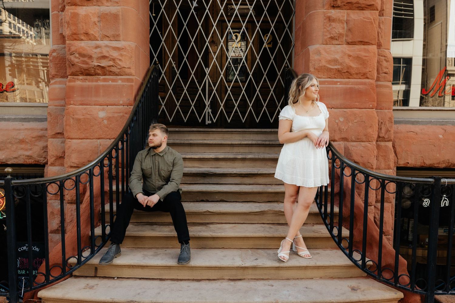 Couple posing on historic red stone steps in formal wedding attire during outdoor photo session.