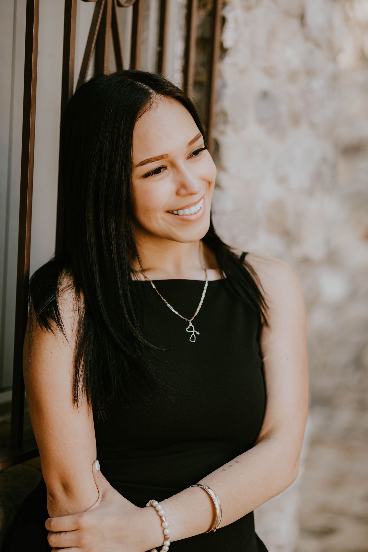 A graduate in a black top smiles while wearing a silver necklace.