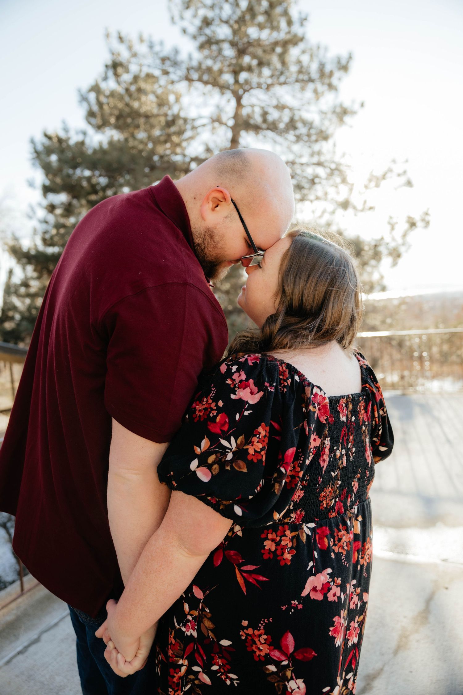 A romantic couple embracing in burgundy and floral outfits against a snowy winter backdrop.