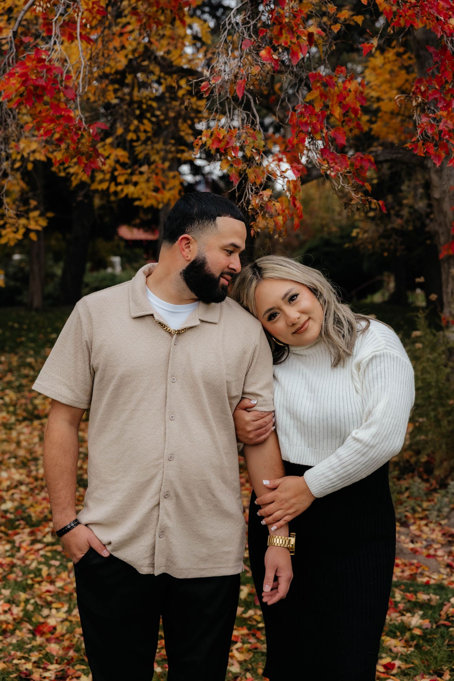Couple sharing intimate moments in an autumn setting with vibrant red and orange fall foliage in the background.