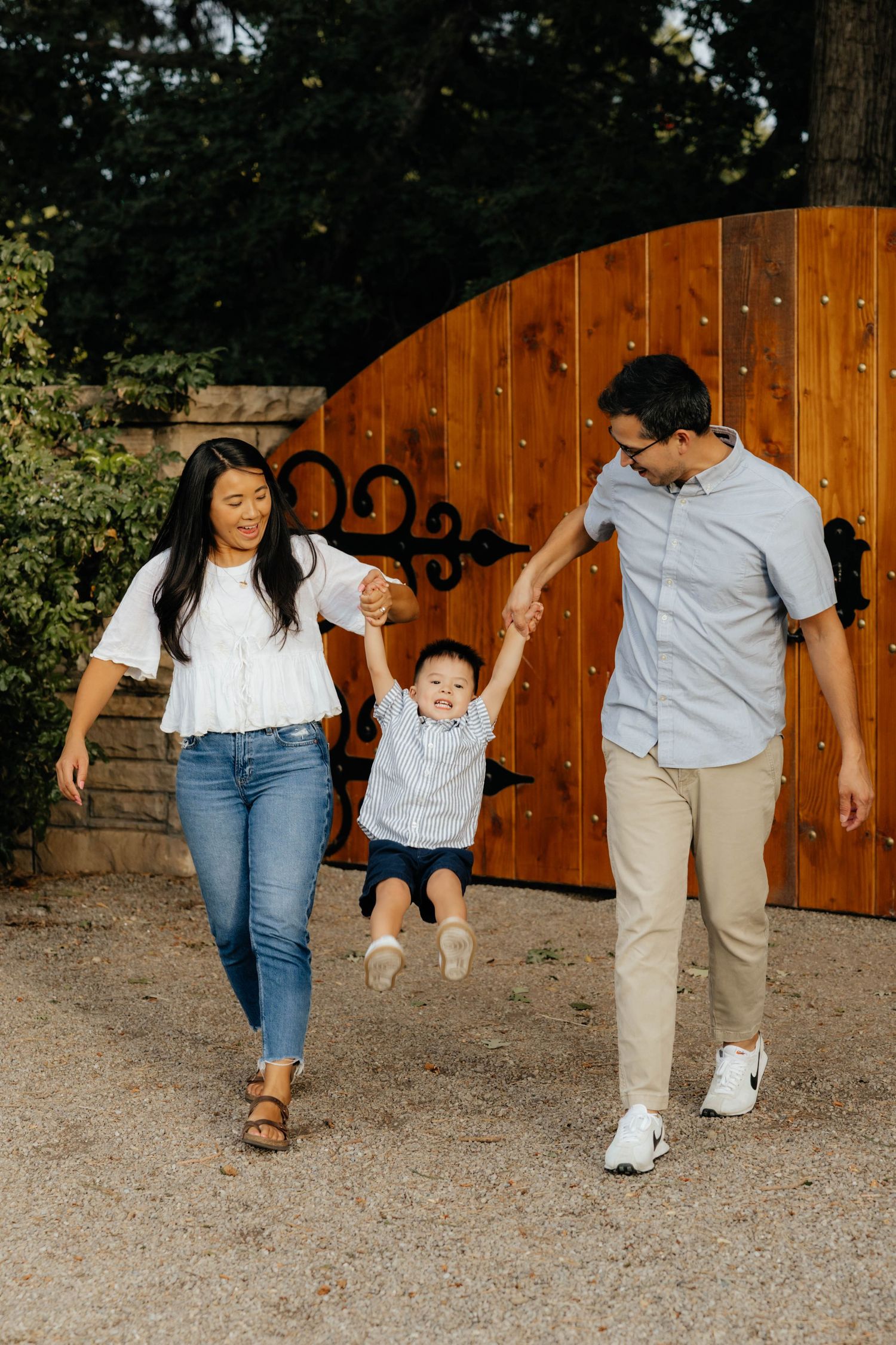 Playful family walking and swinging together in front of a wooden fence.