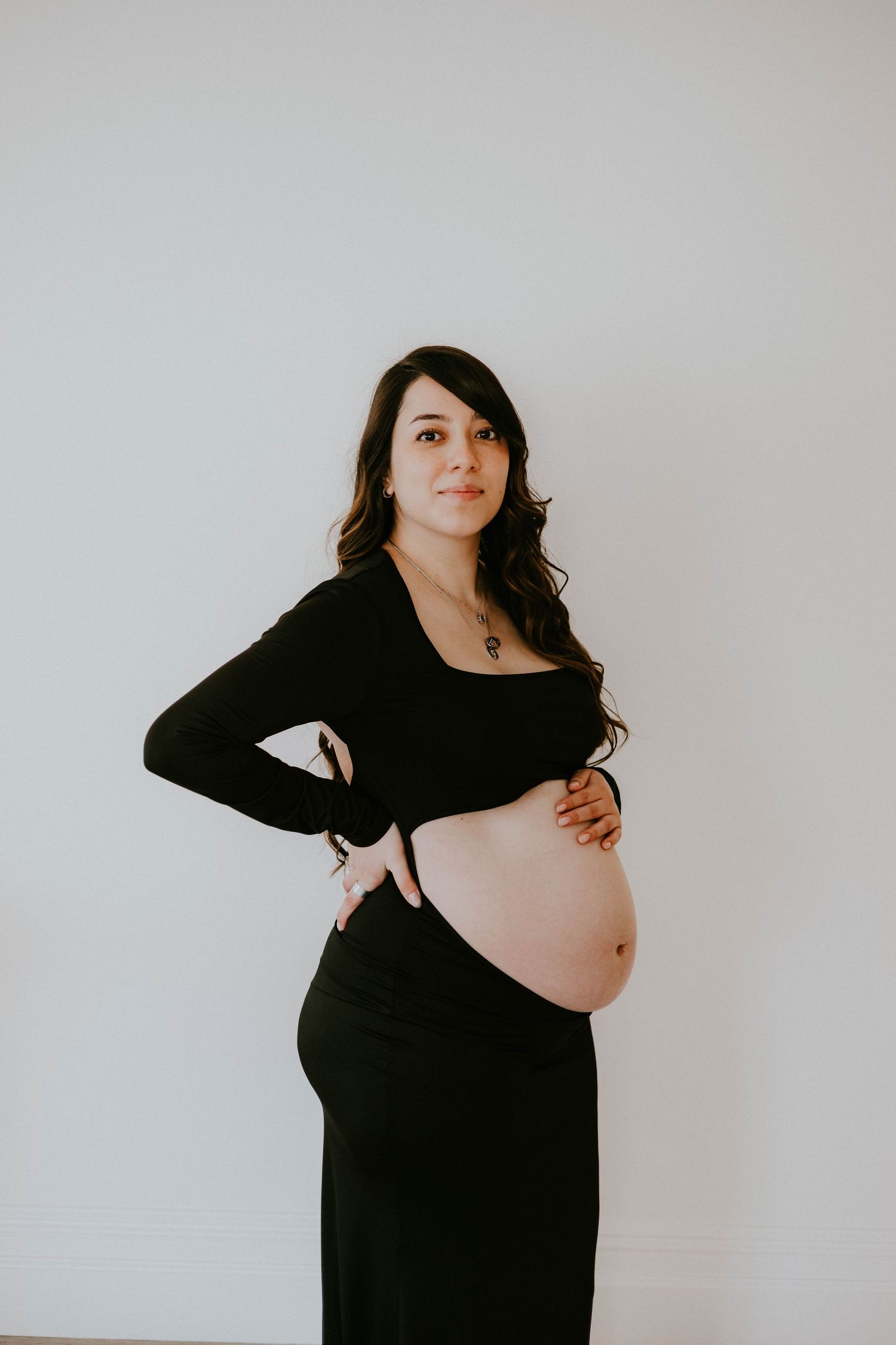 Artistic maternity portraits in black dress against white backdrop.