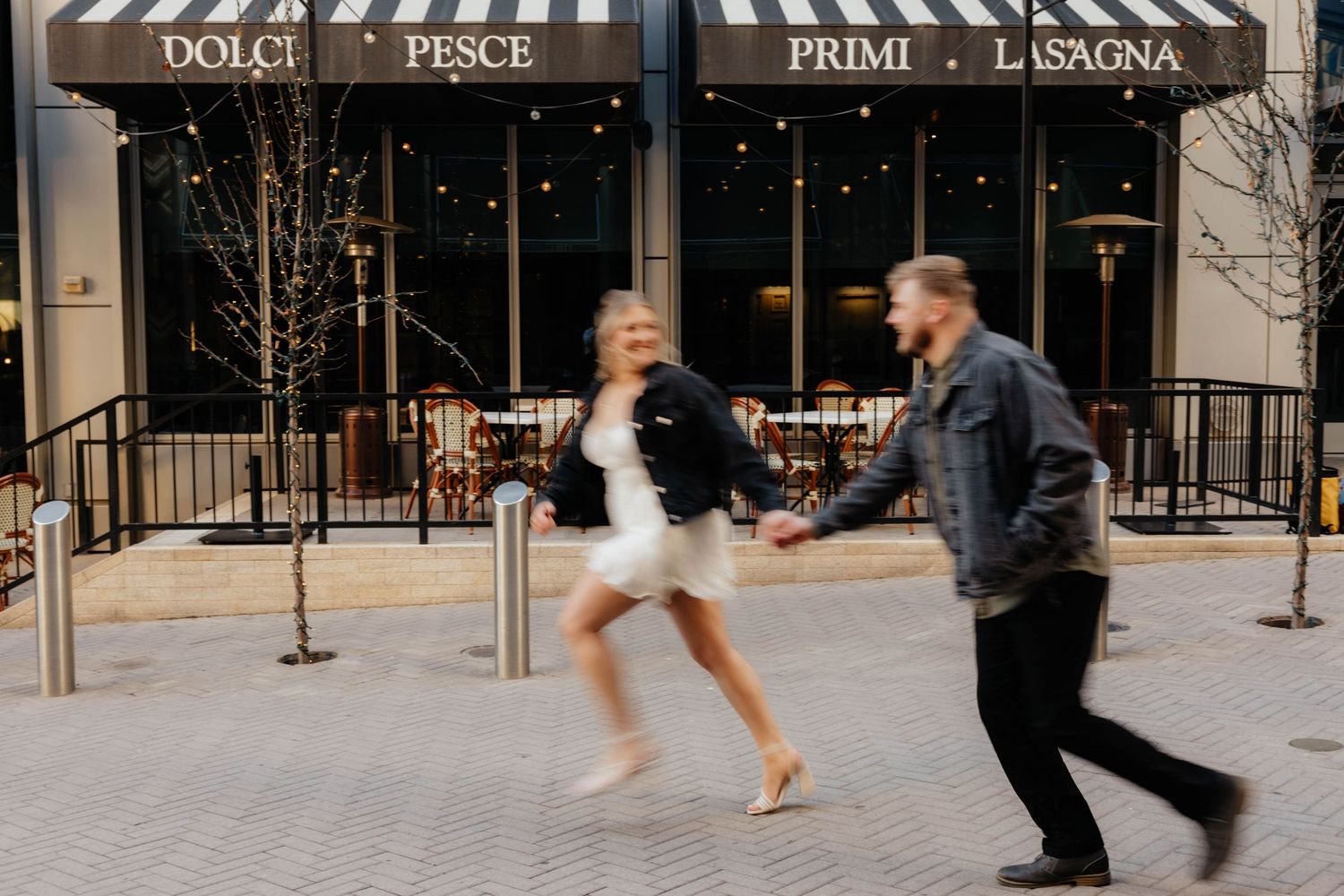 Dancing couple twirling outside restaurant storefront in urban setting.