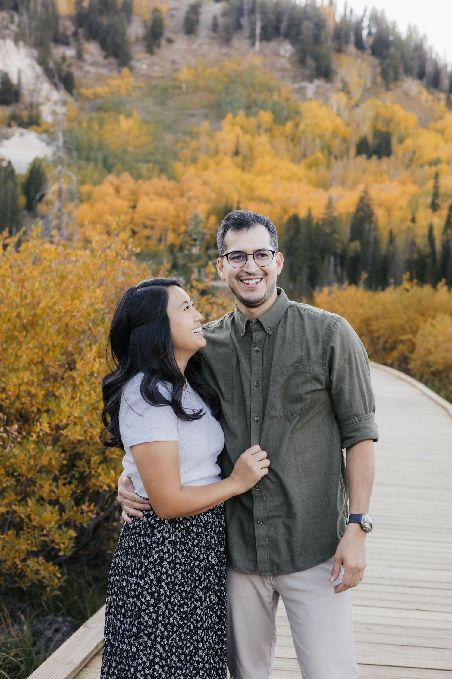 Happy couple posing on wooden boardwalk with autumn mountain landscape in background.