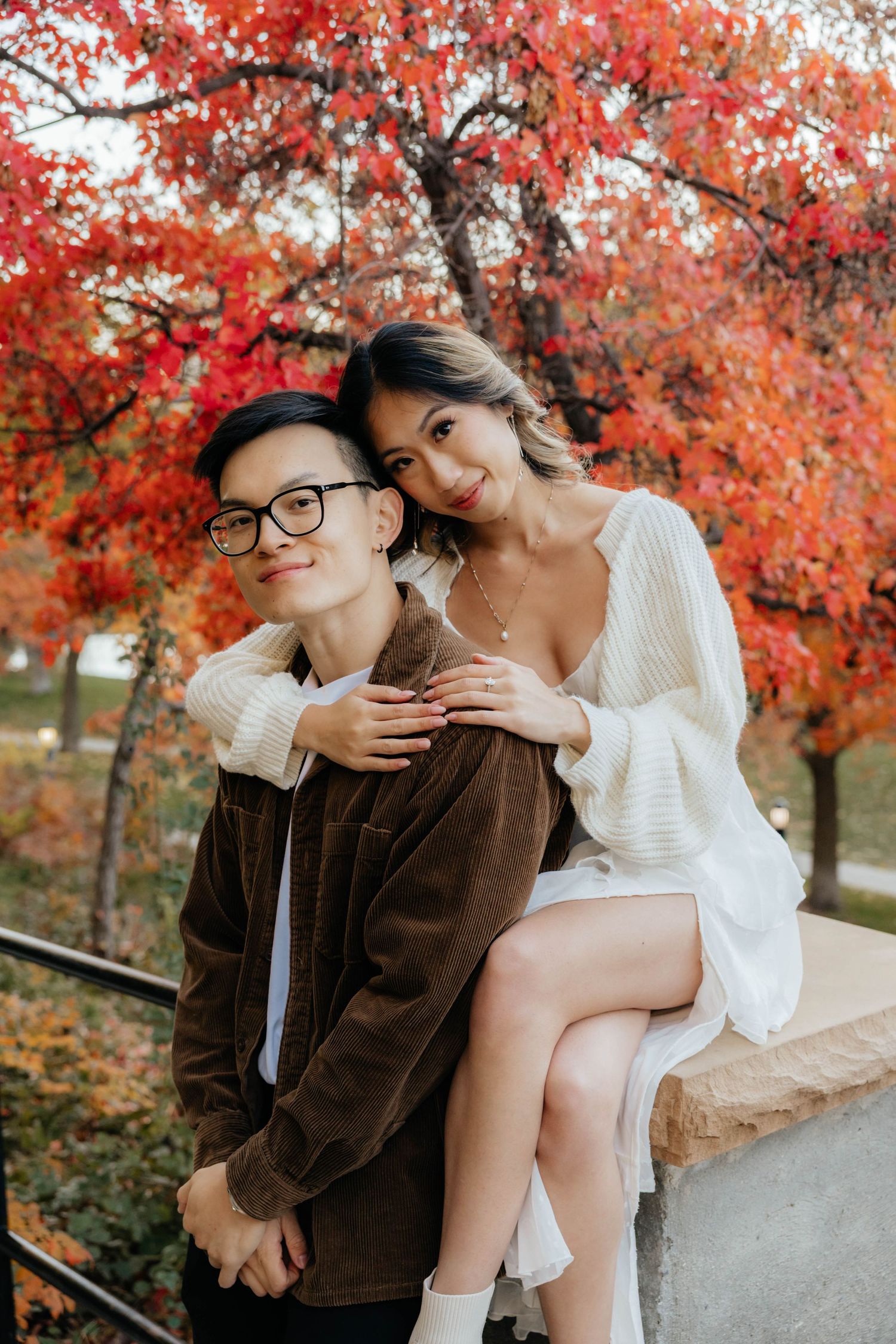 Couple shares playful moments on stone bench surrounded by red fall leaves.