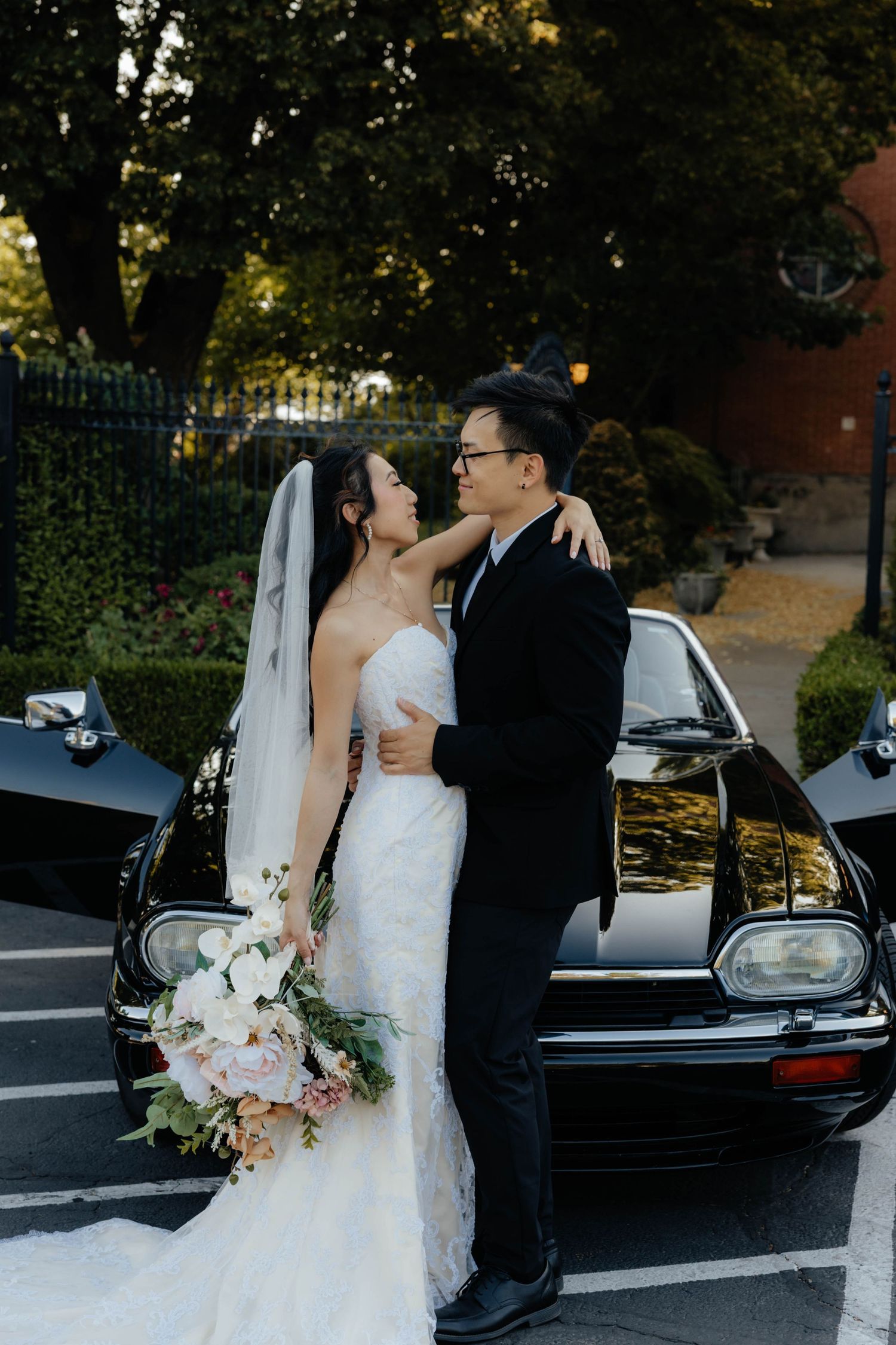 Wedding couple embraces near a classic black car during their photo session.