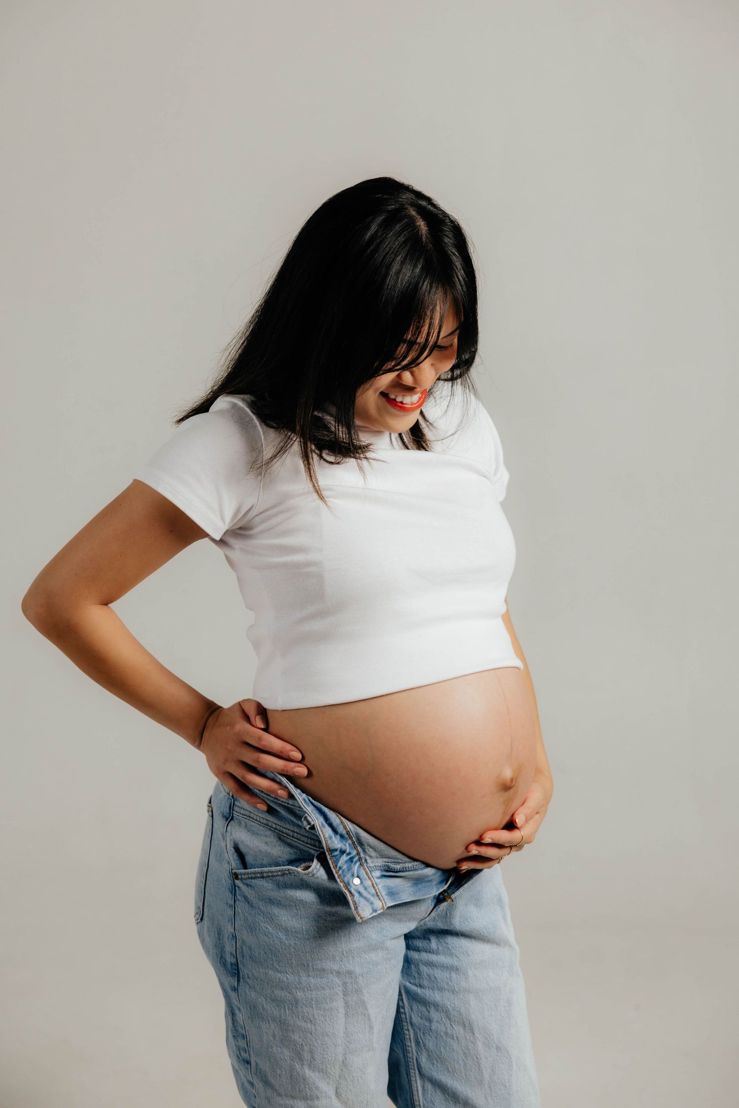 A series of four pregnancy progression photos showing a growing belly while wearing a white top and jeans against a light background.