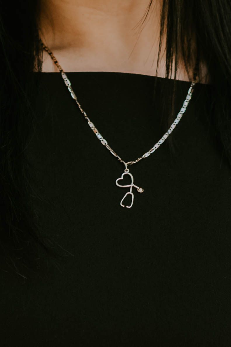 A delicate silver stethoscope charm necklace displayed on a black background.
