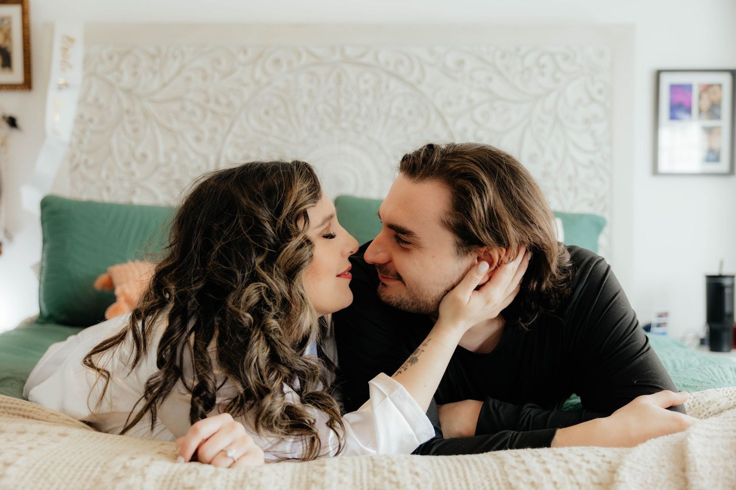 Intimate couple moment on white bedding with decorative wall art in background.