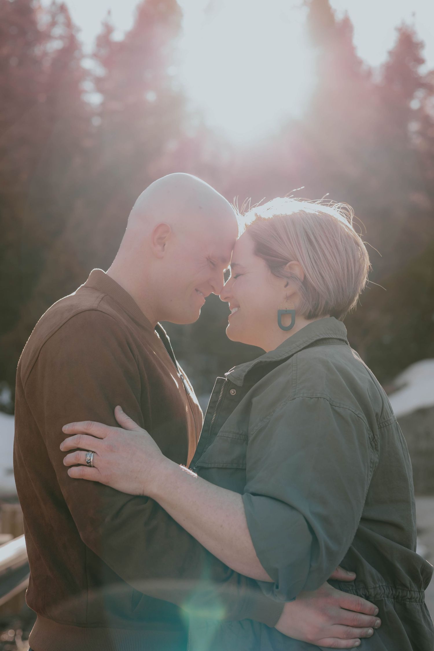 Couple embracing in soft sunset light with pine trees in background.