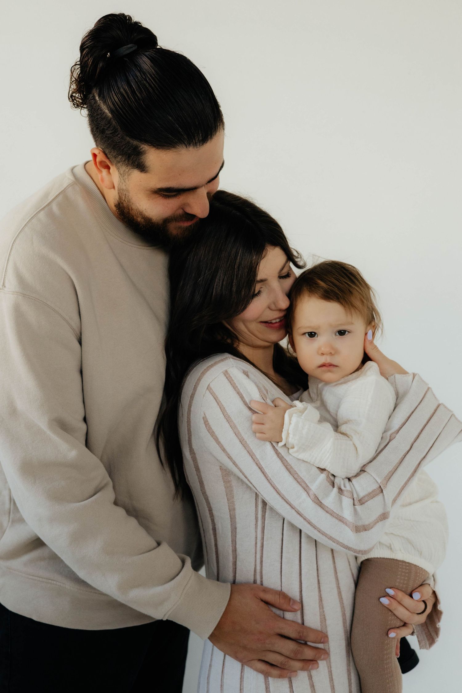 A tender family moment captured in soft neutral tones against a white backdrop.