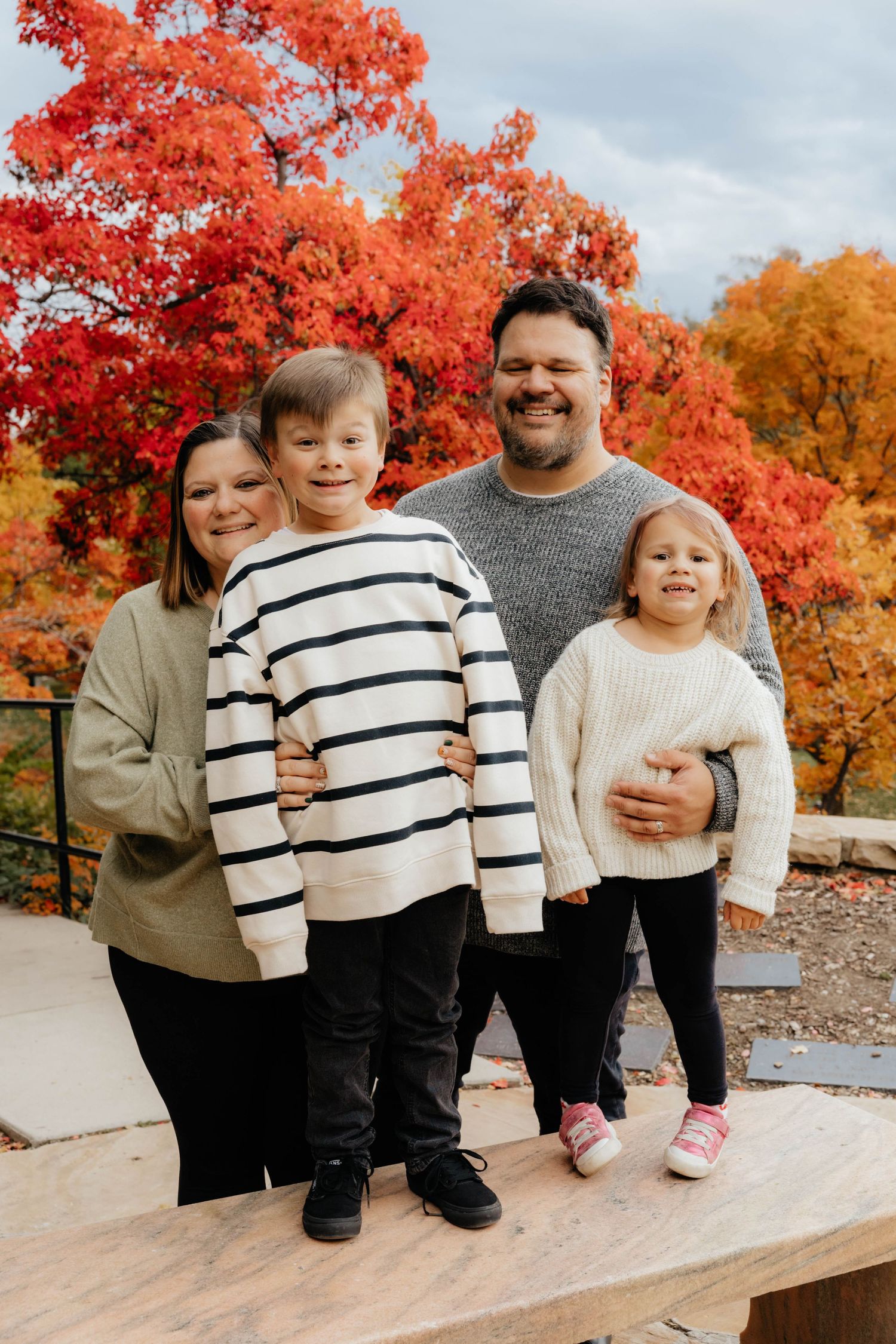 Family portrait on stone steps with vibrant red maple trees in background.