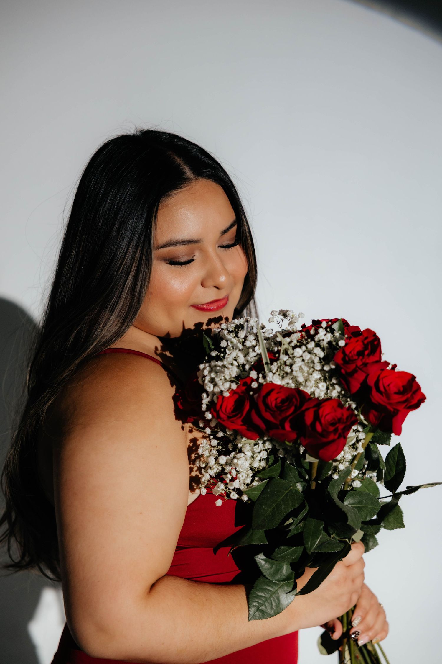 Graduate in red dress holds bouquet of red roses and baby's breath flowers.