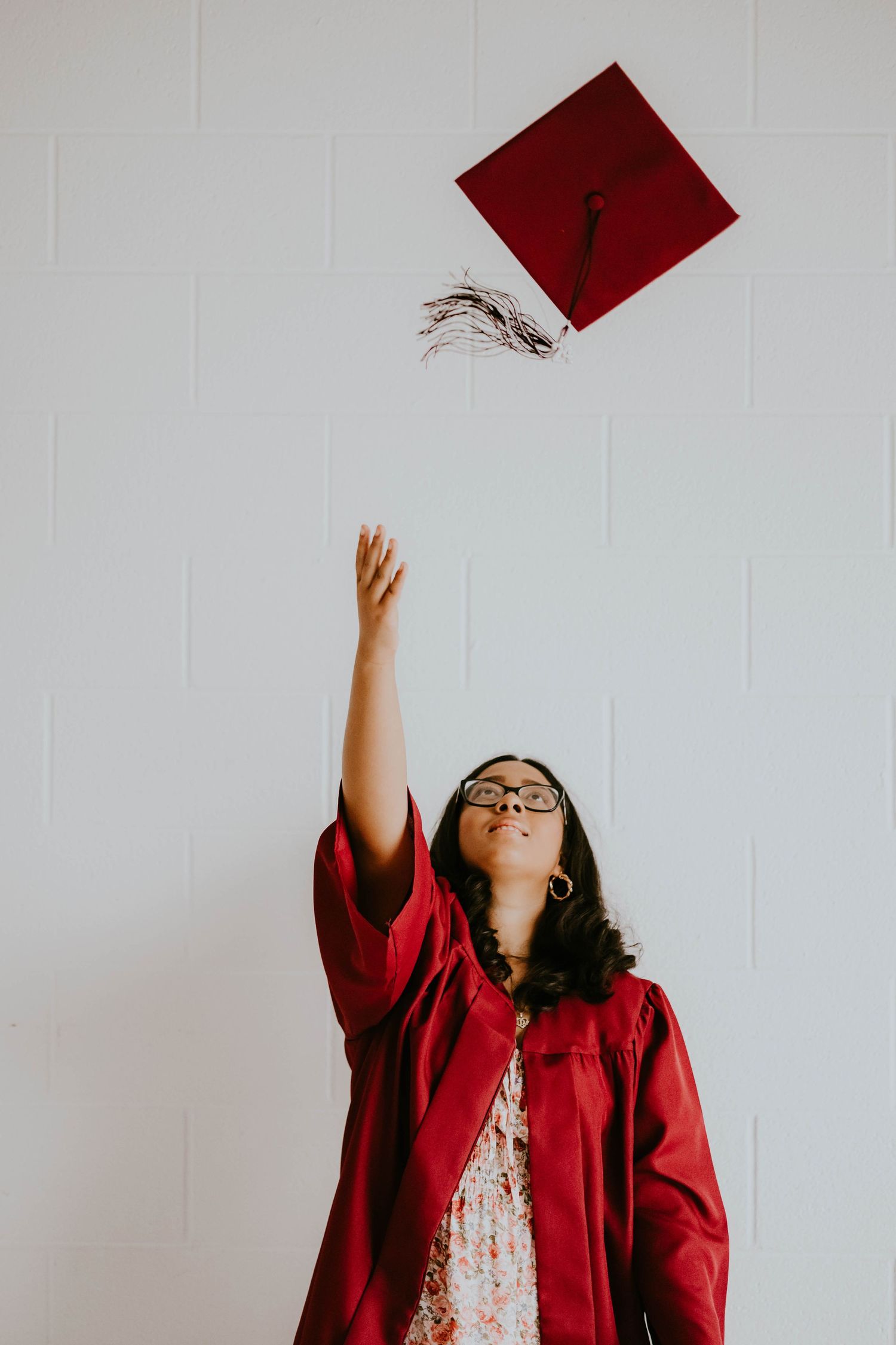 Sequence of graduate tossing red cap in the air against white wall.