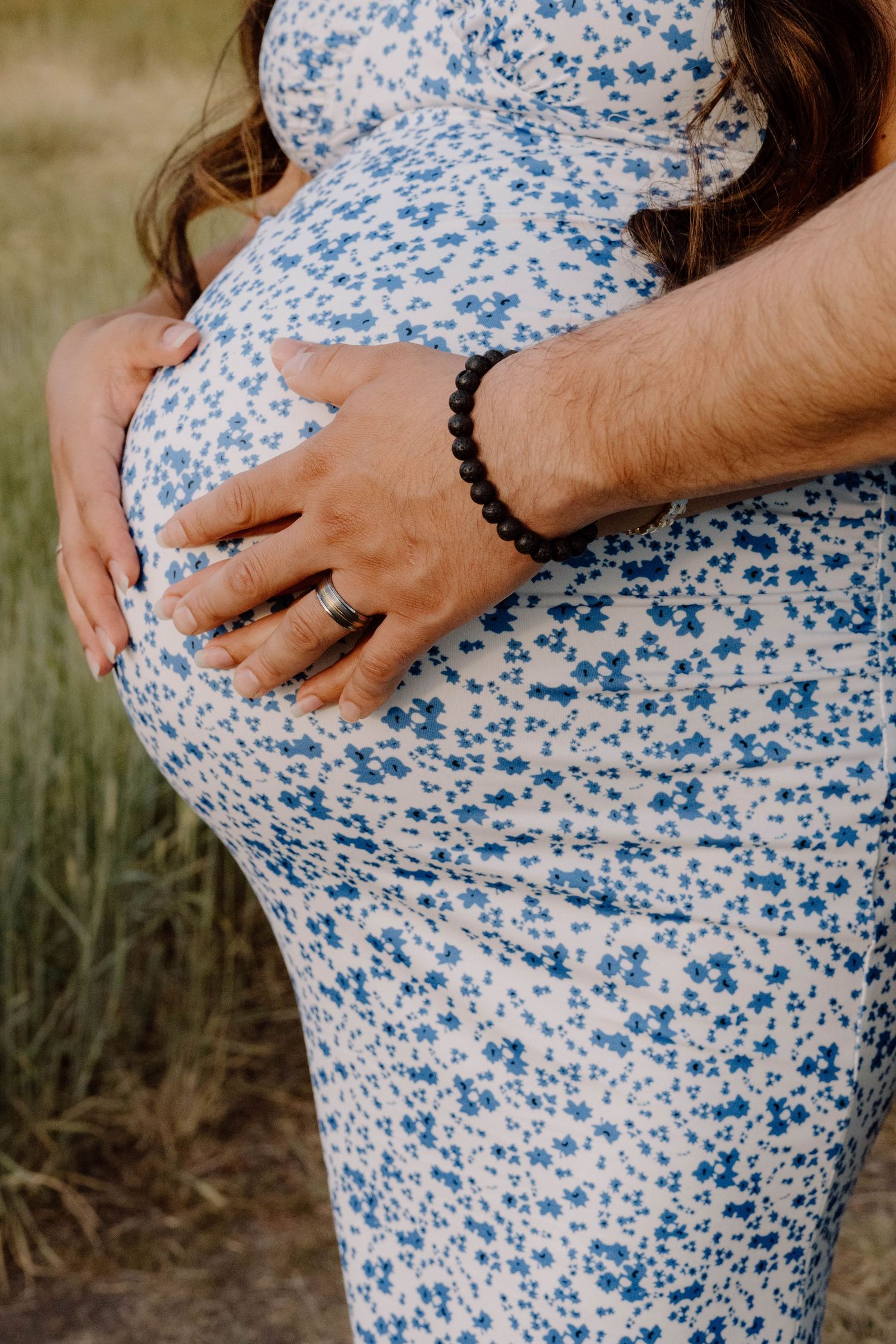 Close-up shots of hands cradling a pregnant belly in a blue floral dress.