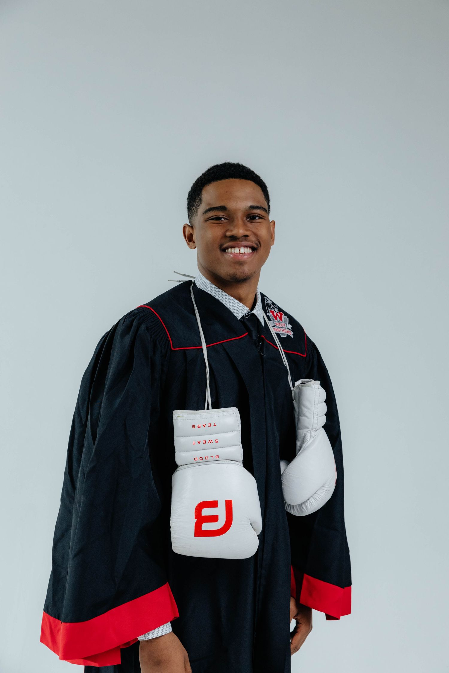 A senior high school student in a studio posing with his cap and gown and boxing gloves