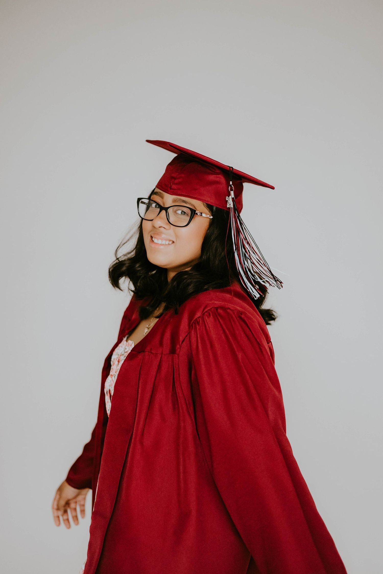 Graduate posing in red graduation gown and cap against white background.