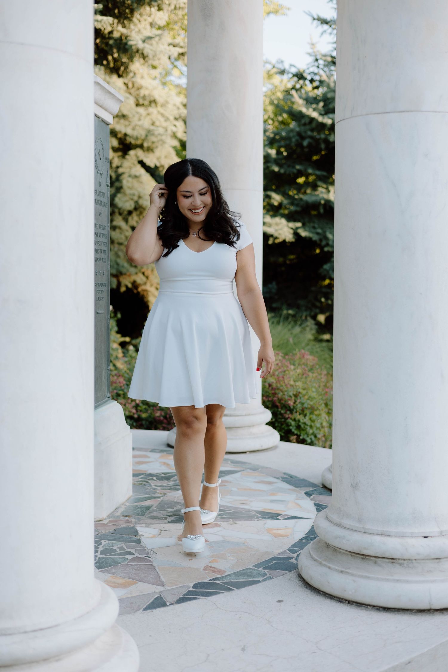 Artistic graduation photoshoot with white dress among classical columns in natural light.