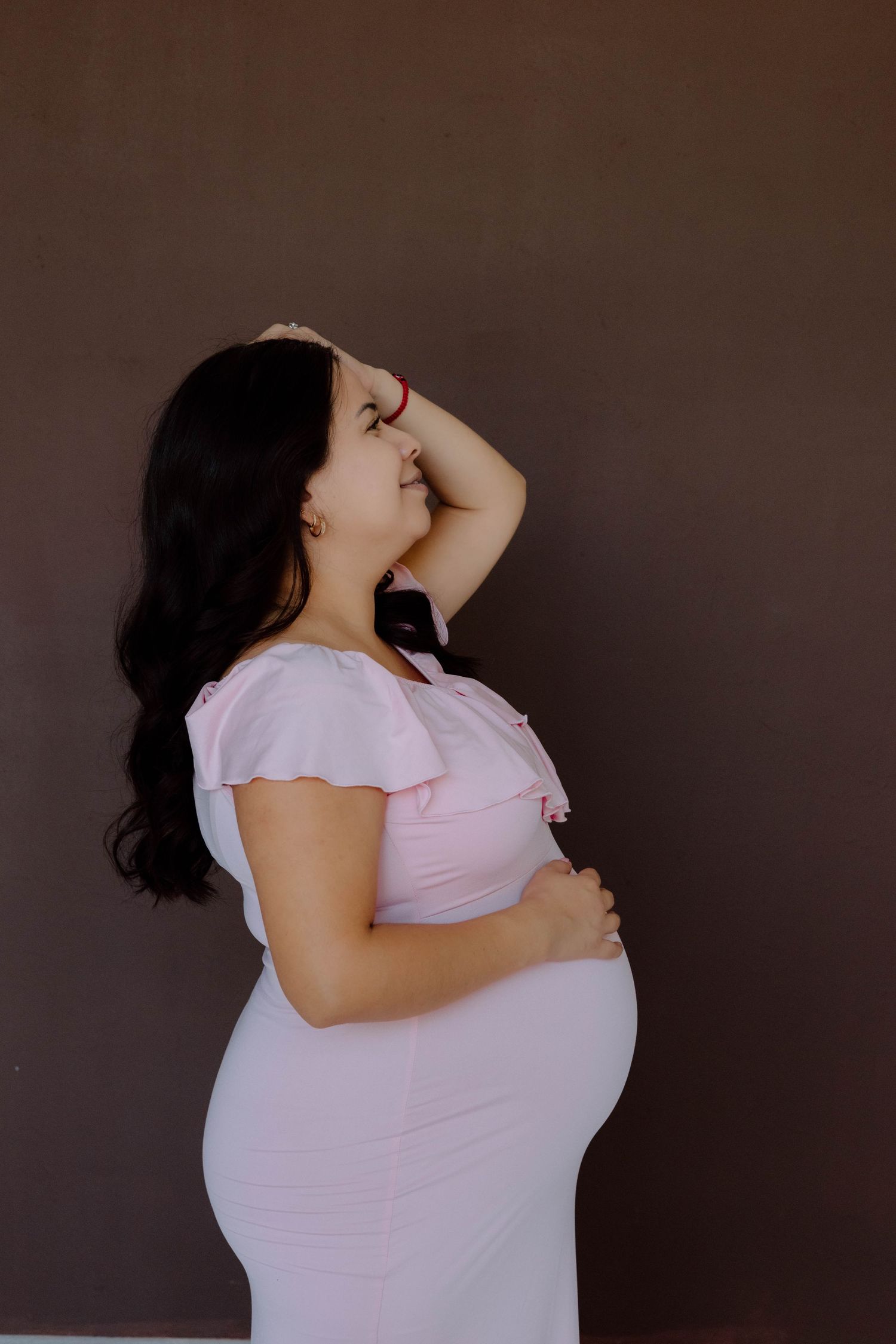 Maternity photoshoot featuring a woman in a pink dress against a dark background.