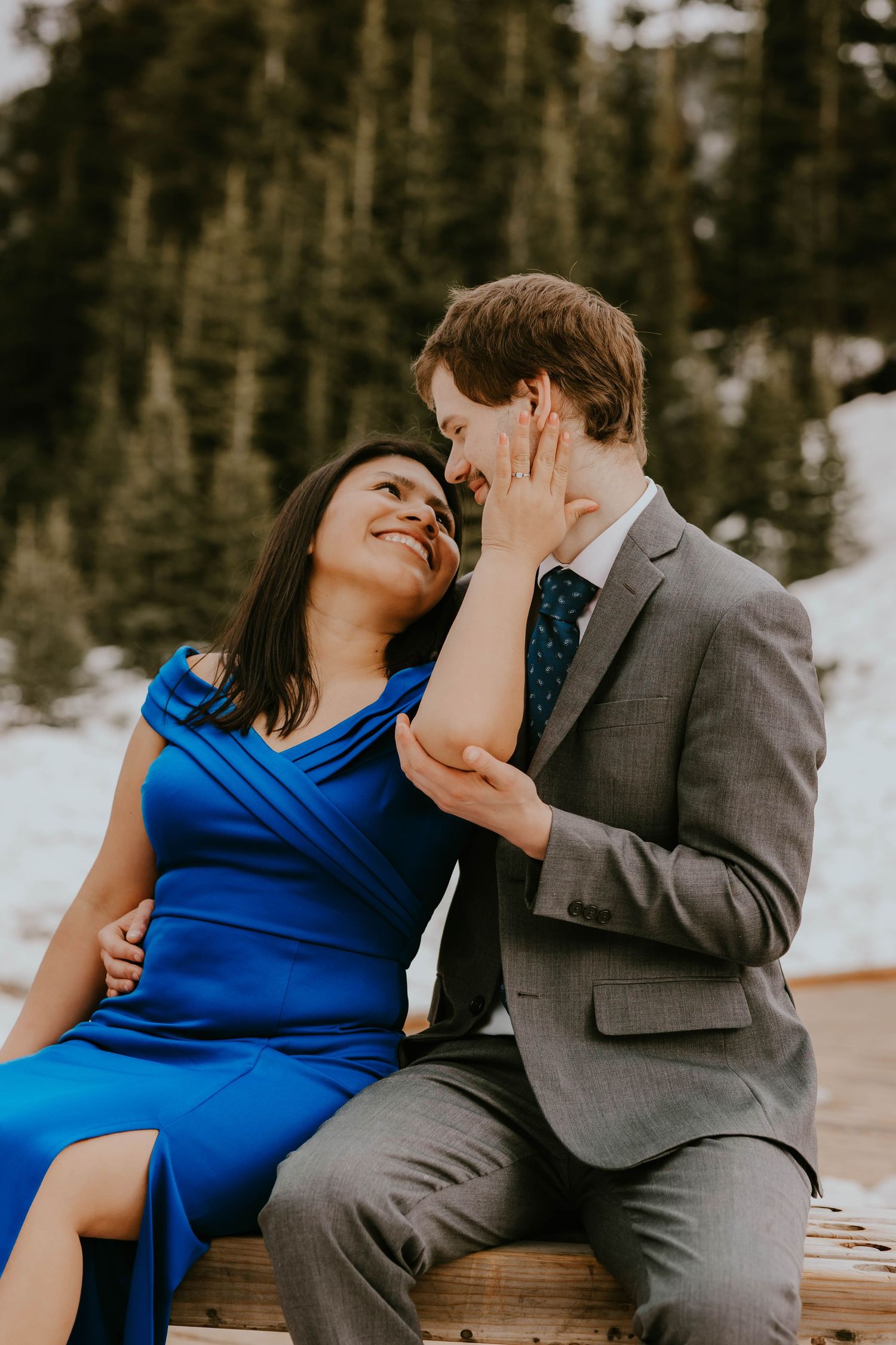 Romantic couple in formal attire sharing tender moment on snowy mountain bench.