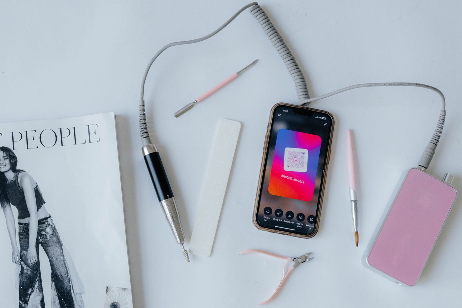 Flatlay of phone, pens, magazine and pink power bank on light gray surface.