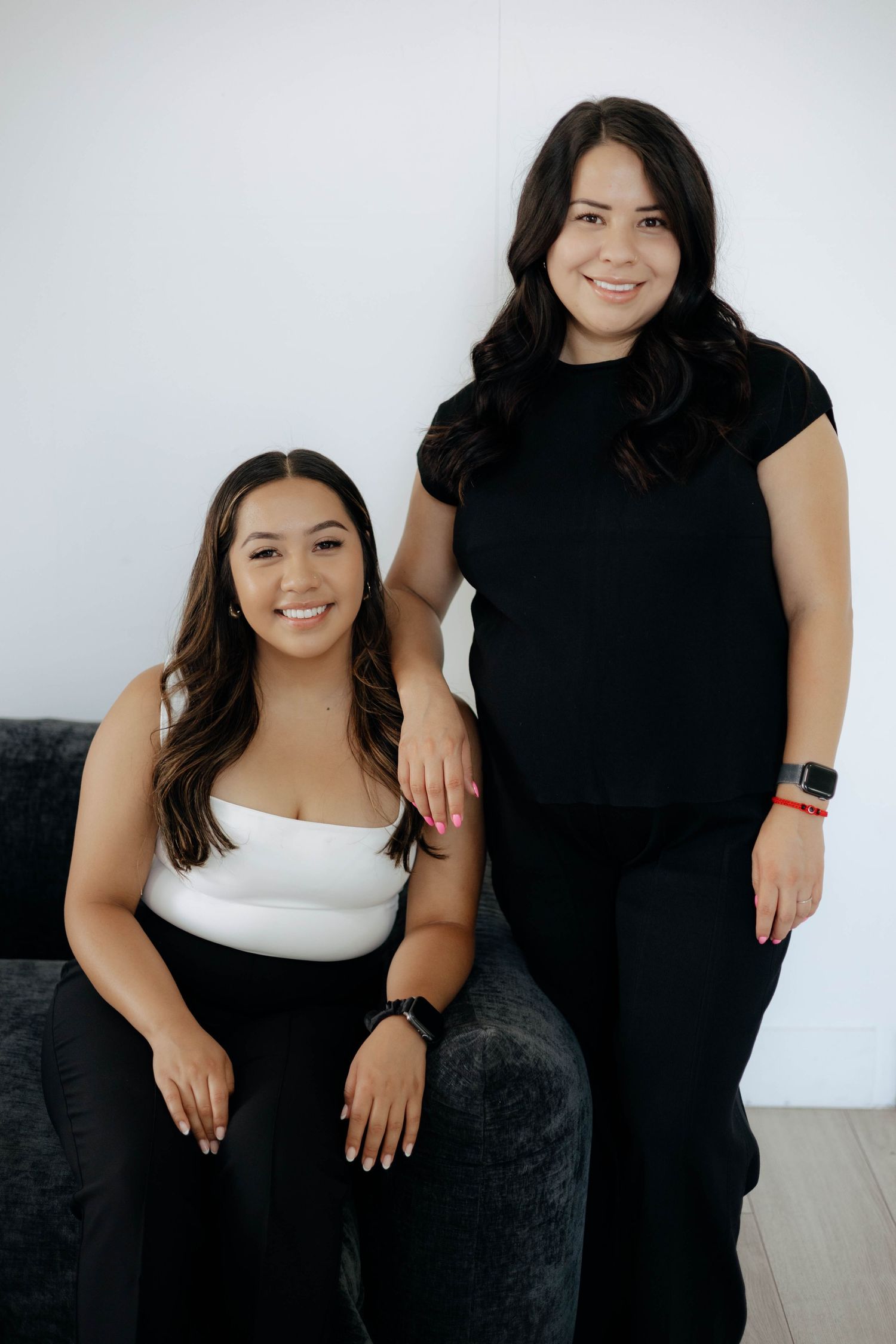 Two people wearing black and white outfits pose together against white background.