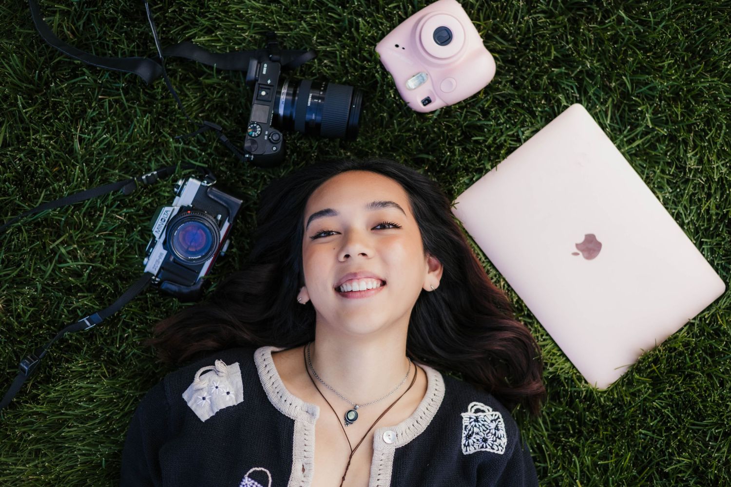 Overhead shot of photographer lying on grass with cameras and laptop.