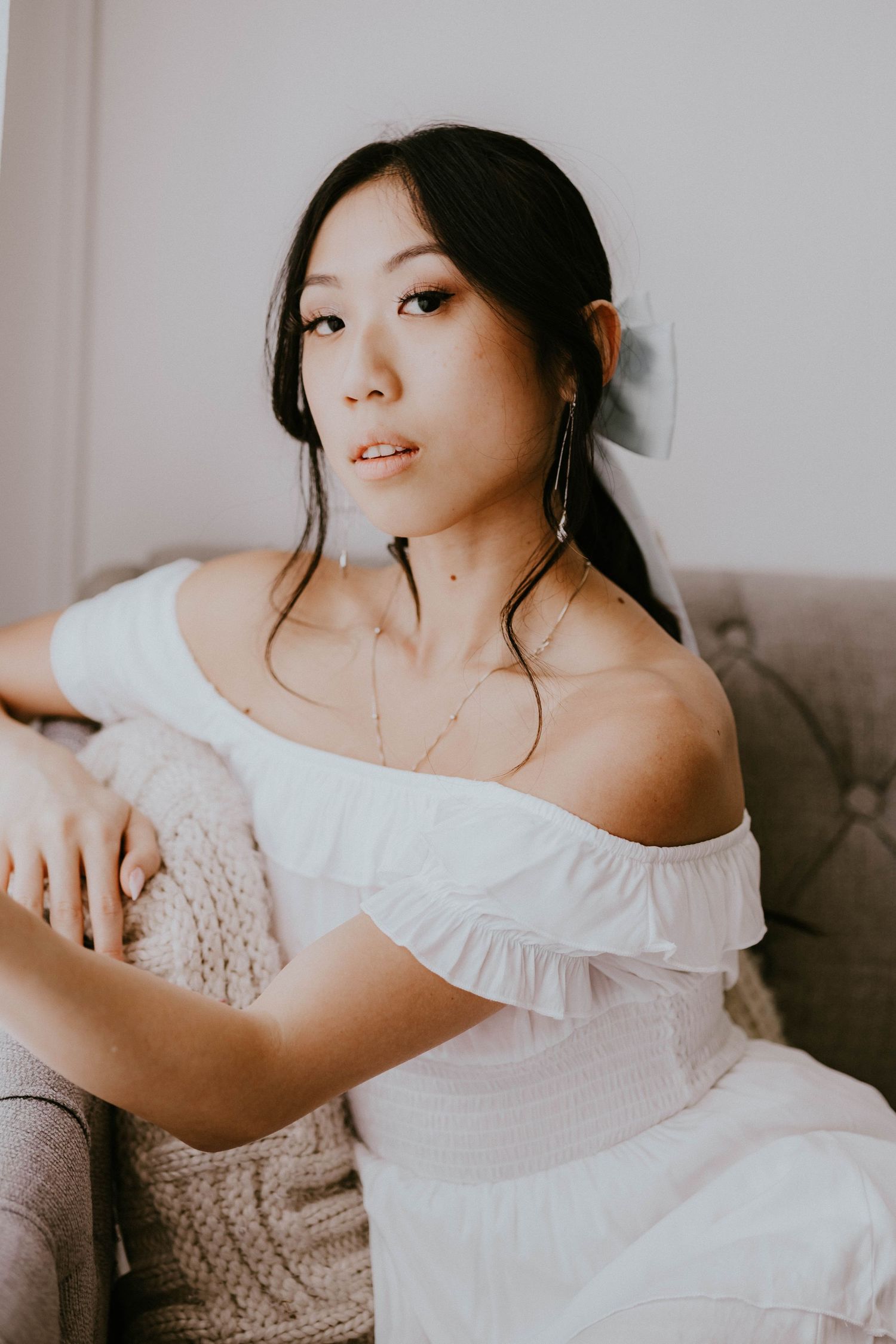 Casual lifestyle portrait on couch wearing white off-shoulder top.